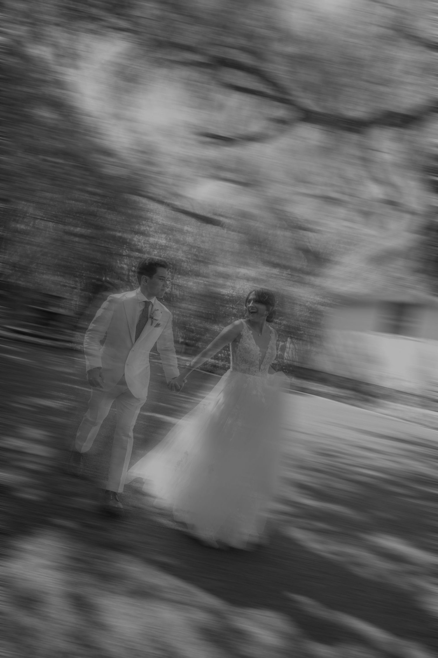 Bride and groom hold hands walking in a dreamy motion-blur black and white wedding photo.