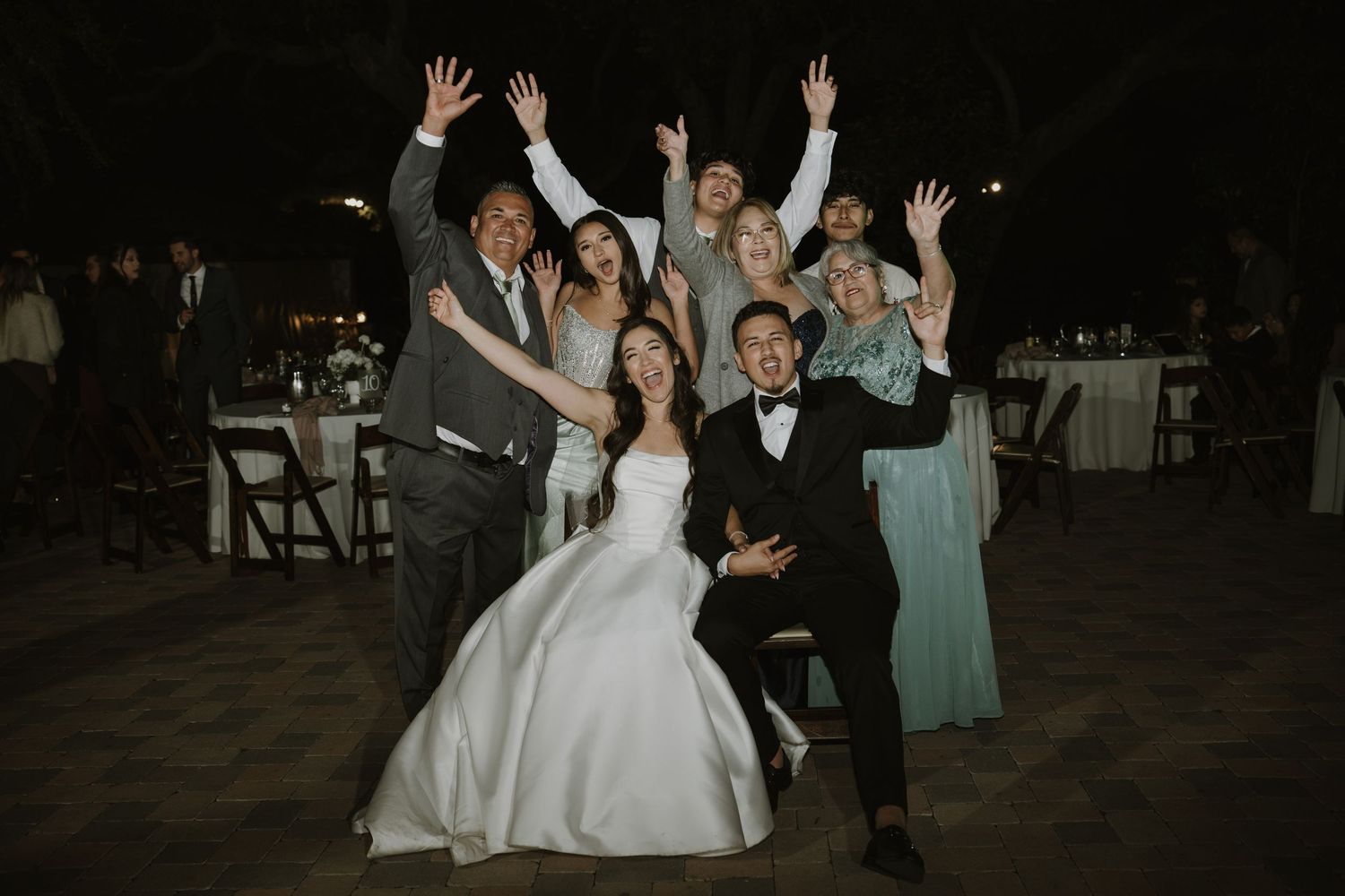 Wedding guests and couple raise their hands in celebration during an evening reception dance.