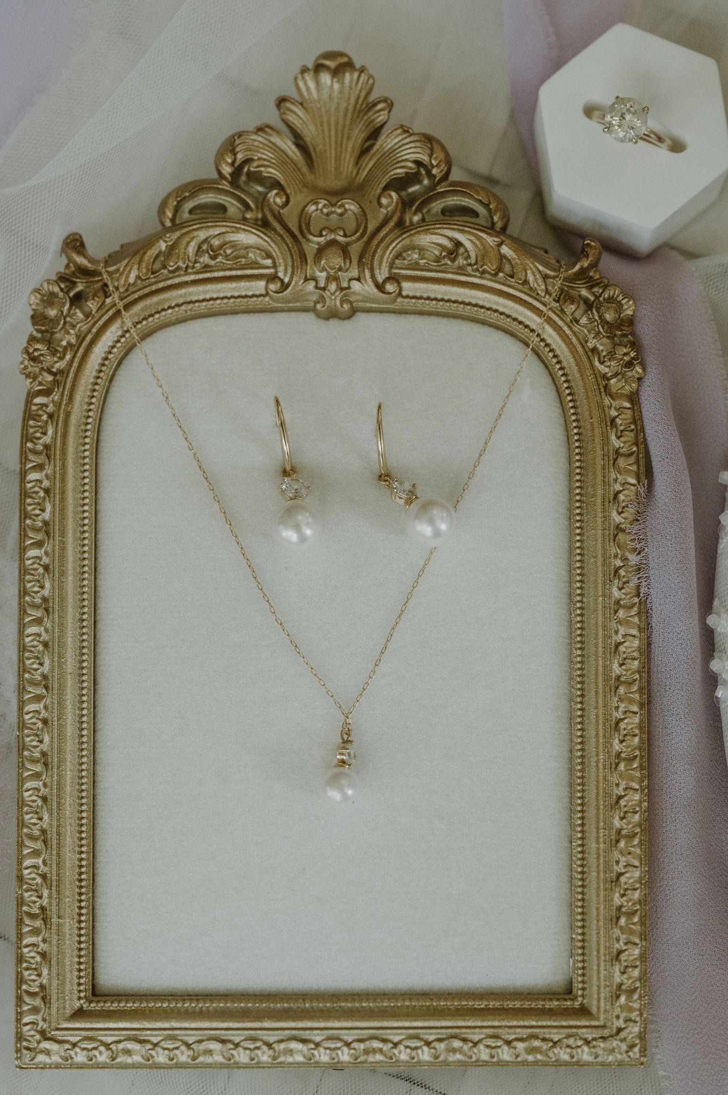 Elegant gold vintage frame displaying delicate pearl wedding jewelry set against white background.