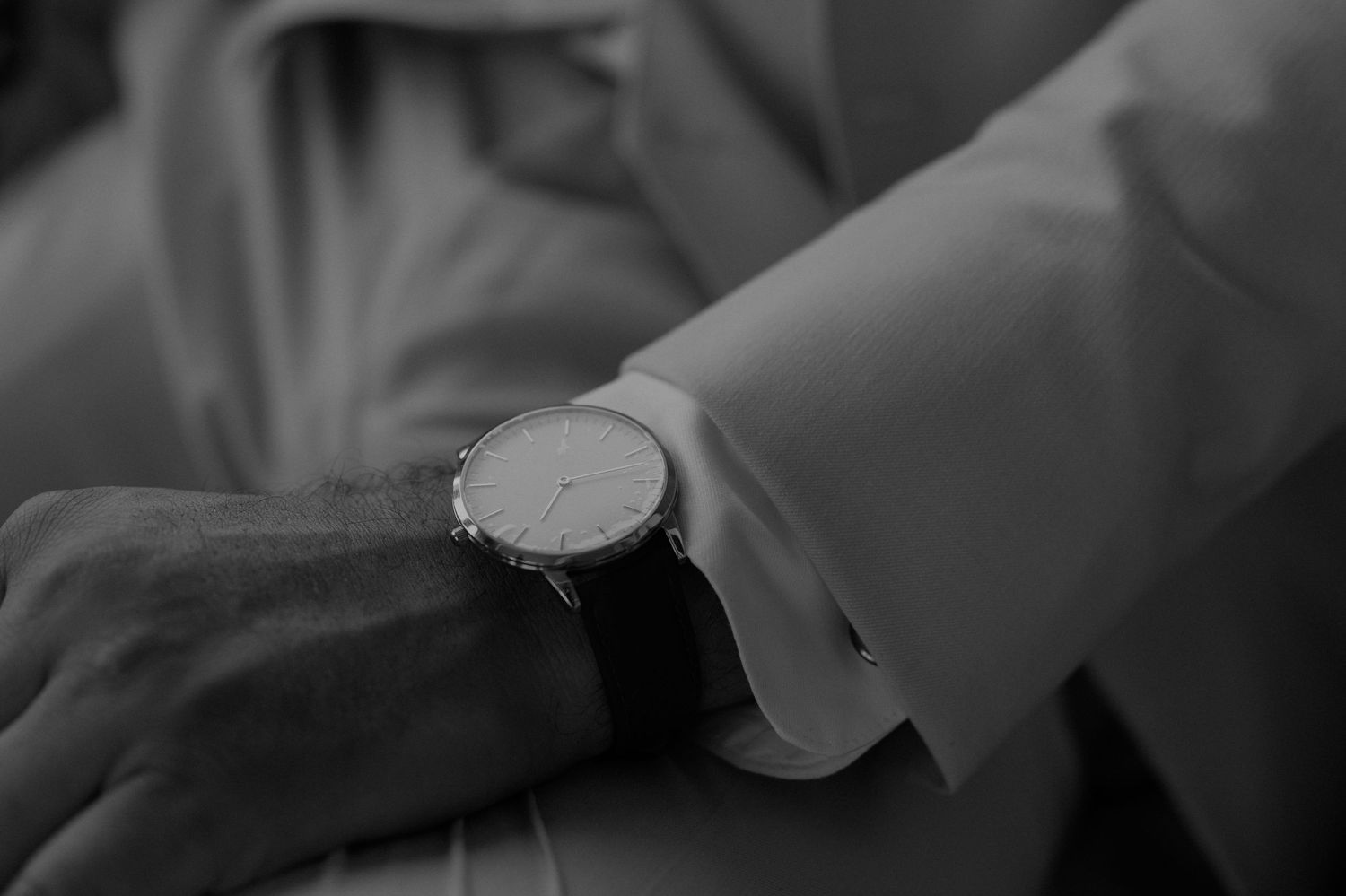 Black and white detail shot of an elegant wristwatch on formal attire.