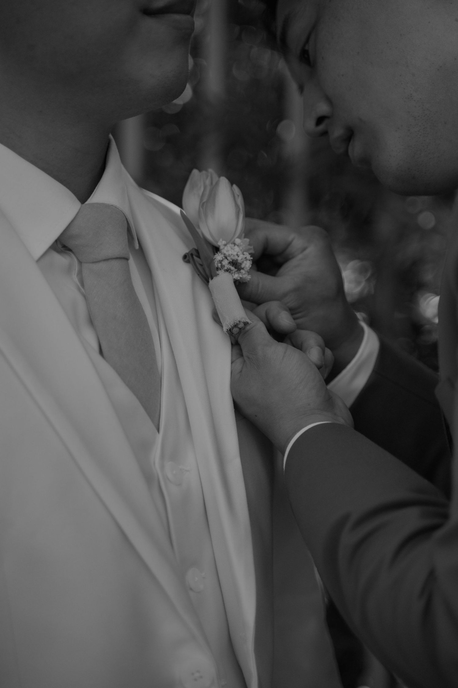 Close-up black and white shot of a boutonniere being pinned to a dress shirt collar.