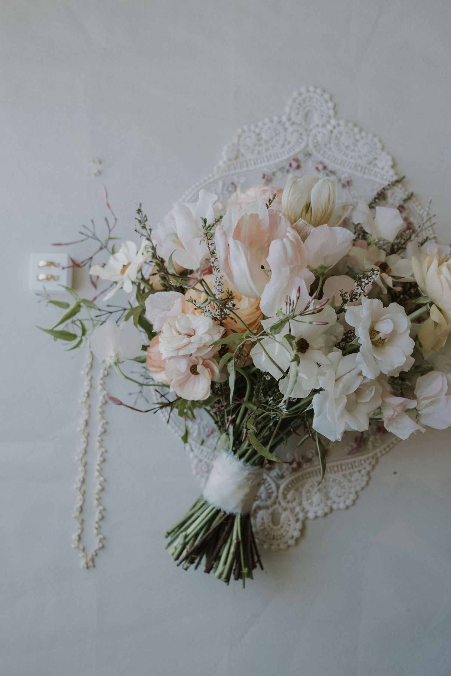 Elegant bridal bouquet of white and blush tulips, sweet peas, and greenery on a lace doily.