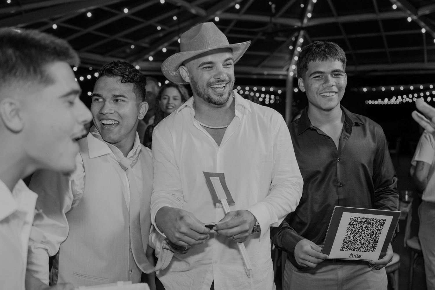Group of men in white attire smiling and celebrating at an outdoor wedding reception event.