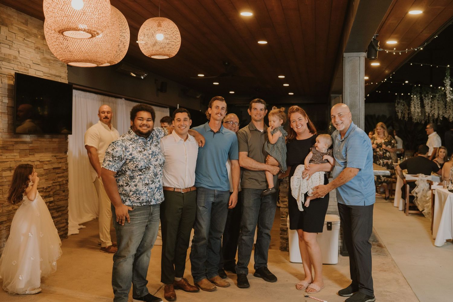 Group of wedding guests smiling and posing together indoors at a reception venue with warm lighting.