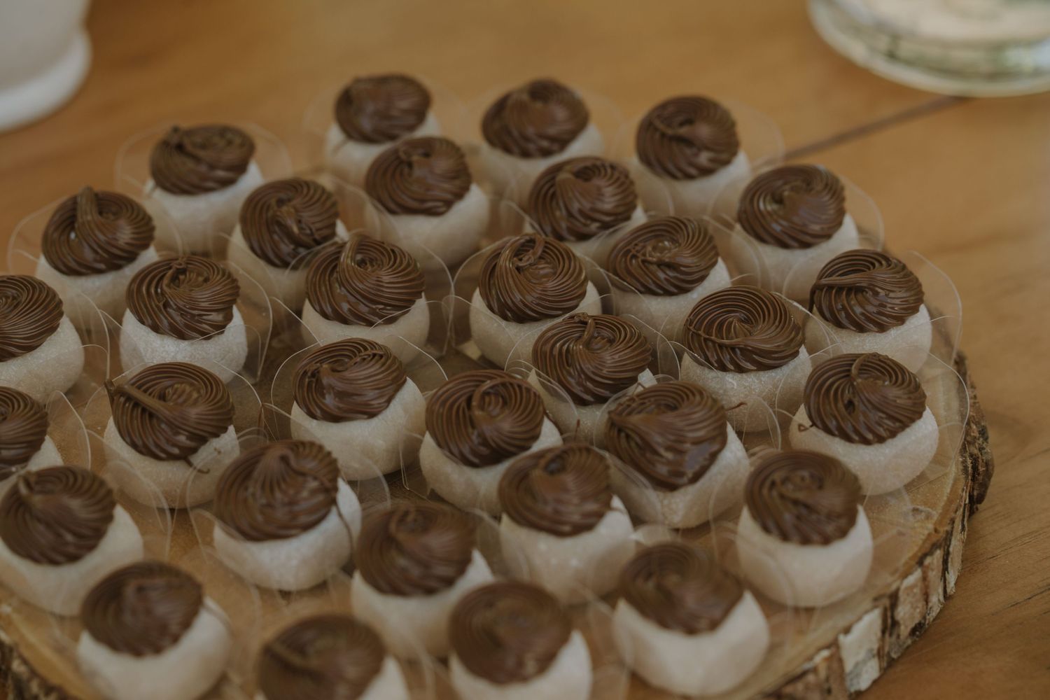 Elegant white cake pops topped with swirled chocolate frosting arranged on a rustic wooden board.