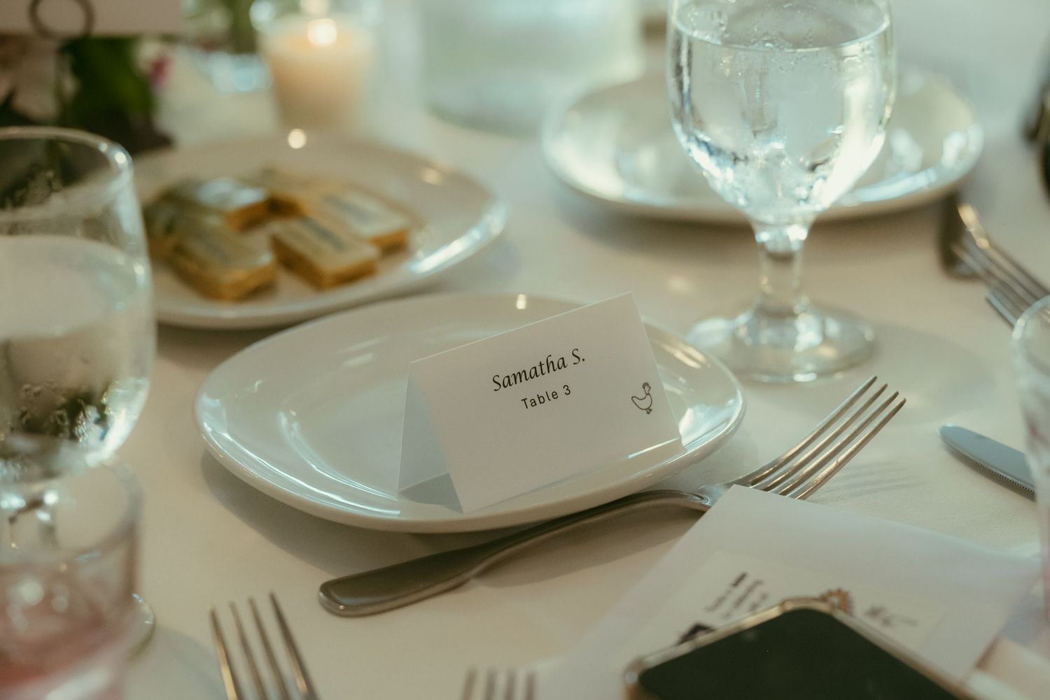 Elegant wedding place setting with personalized name card, white plate, crystal glassware, and silverware.