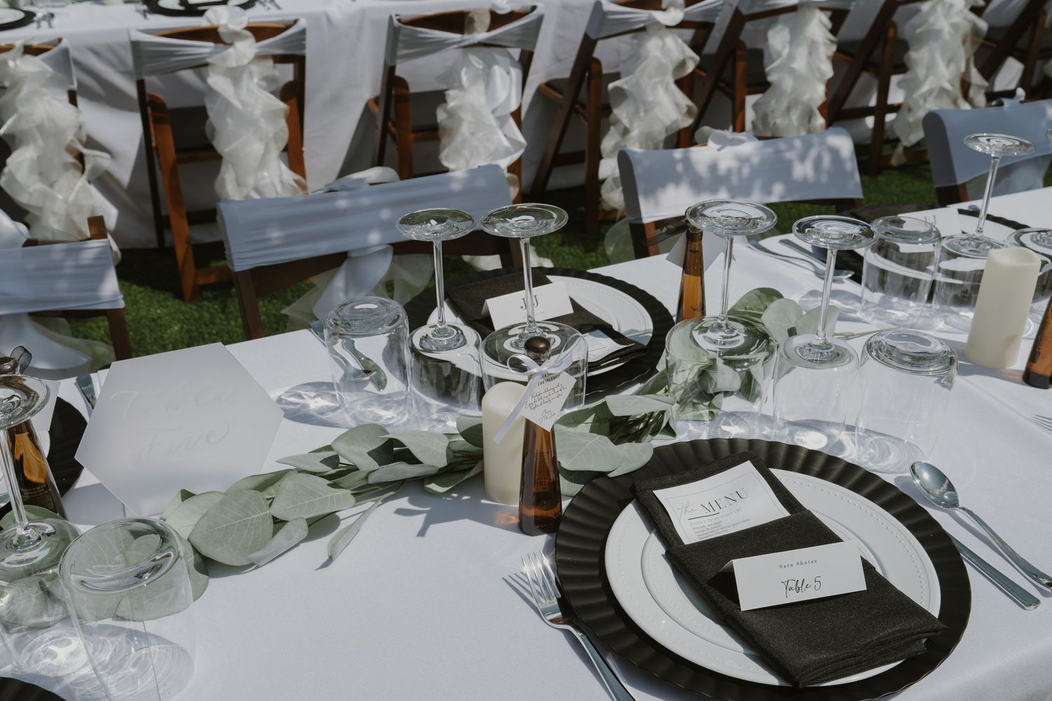 Elegant wedding reception table setting with black charger plates, eucalyptus greenery, and white linens.