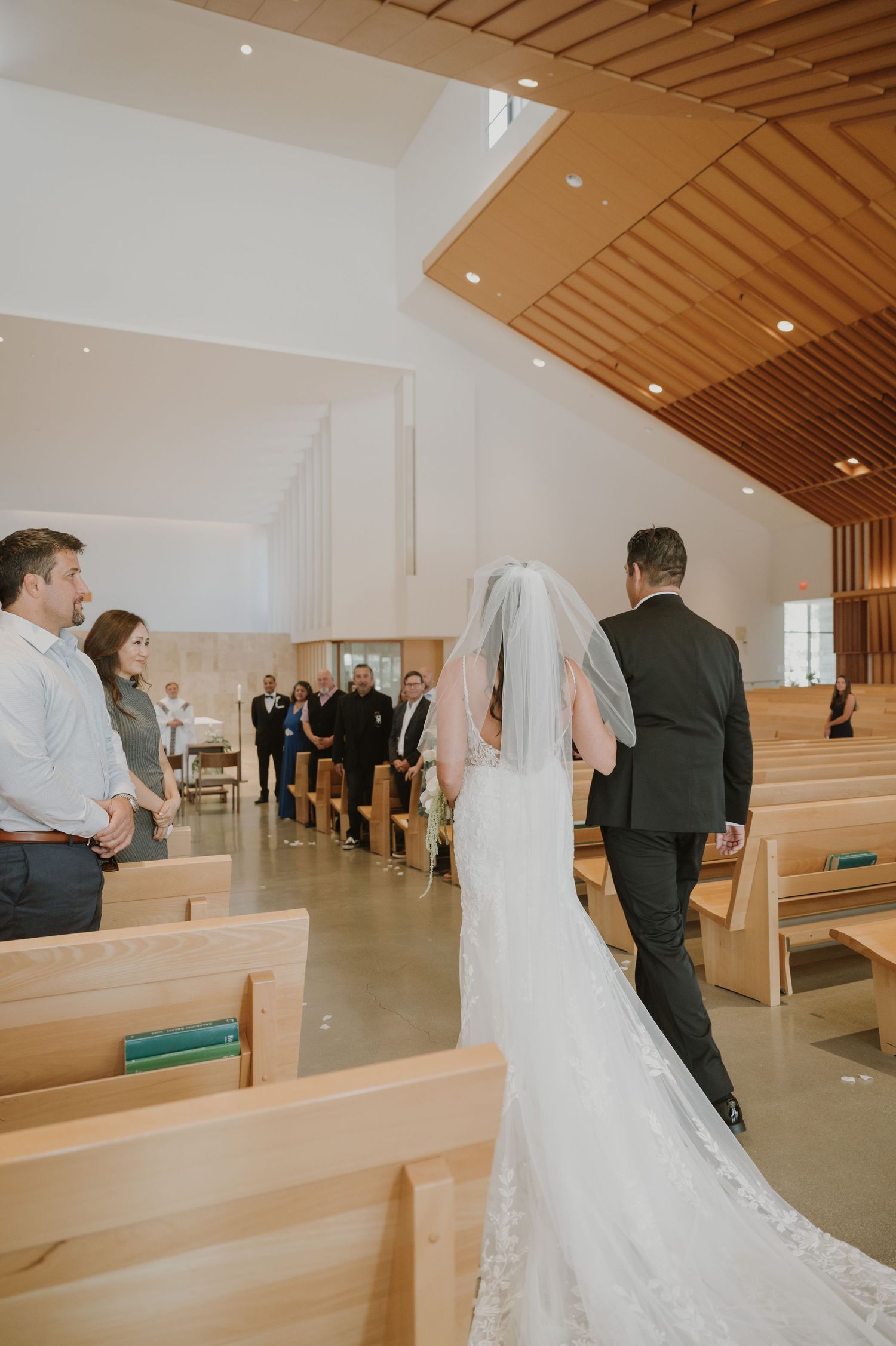 Bride walking down the aisle in a white gown and veil at a modern church wedding ceremony.