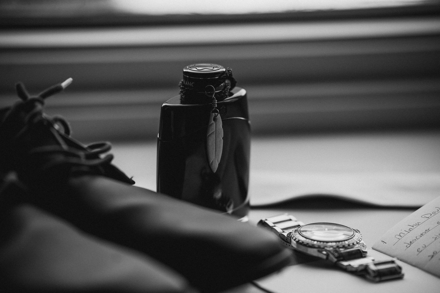 Black and white flat lay of mens wedding accessories including dress shoes, cologne bottle, and a watch.
