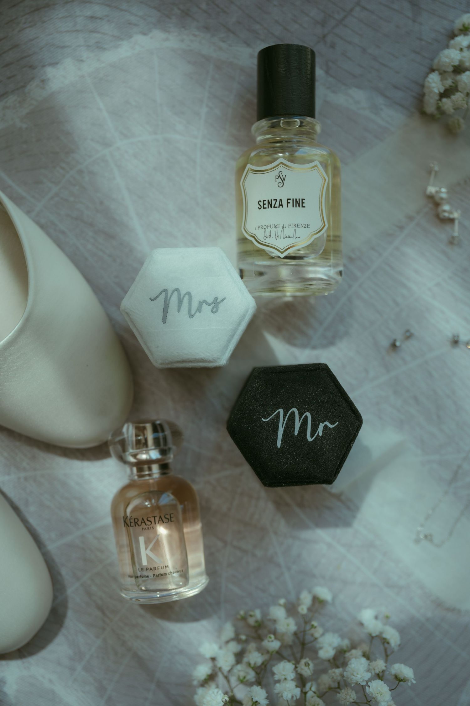 Elegant wedding flat lay with Mr and Mrs ring boxes, Senza Fine perfume, Kerastase fragrance, and white bridal heels.