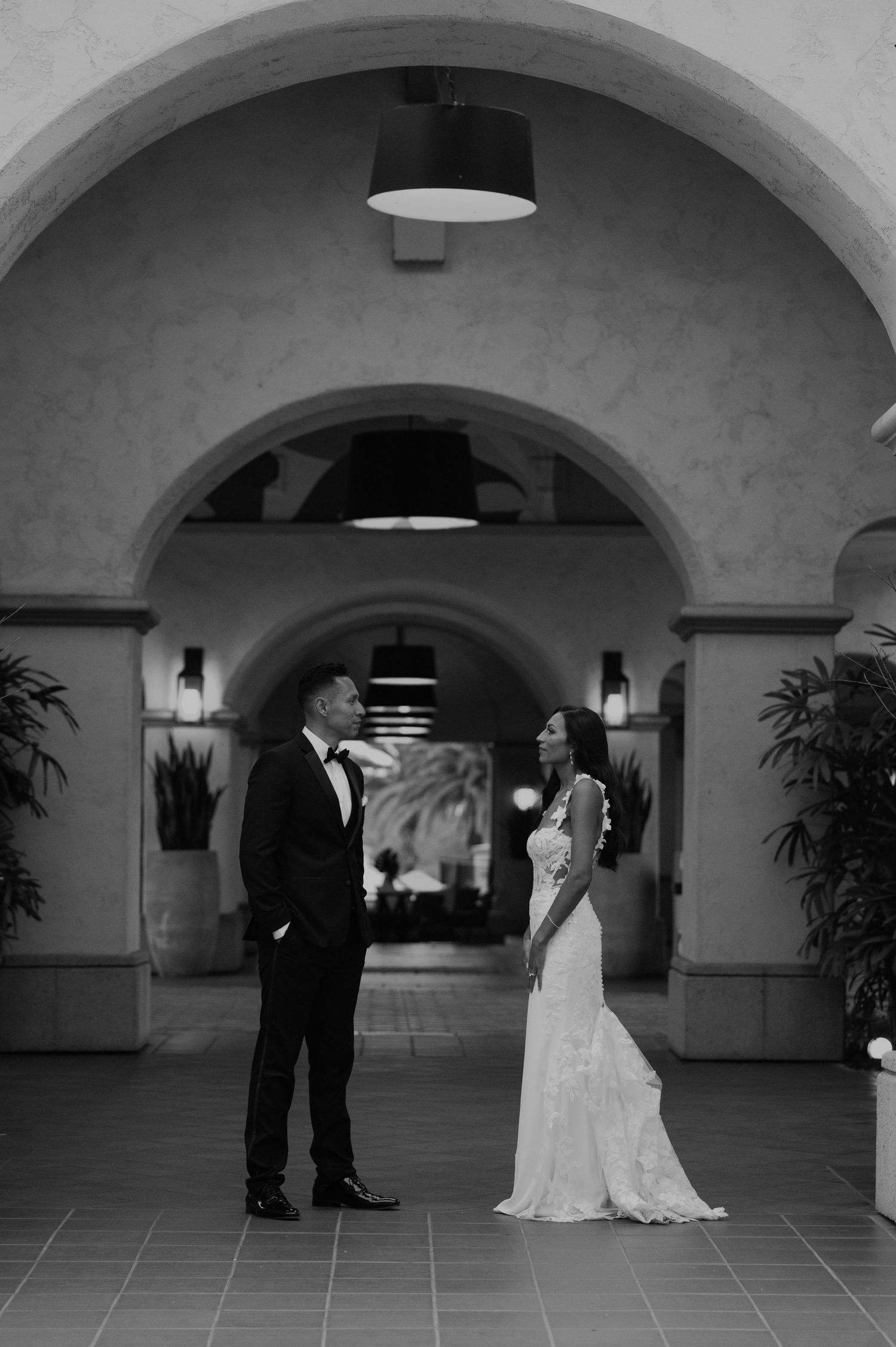 Black and white photo of newlyweds dancing under arched hallways in an elegant venue.