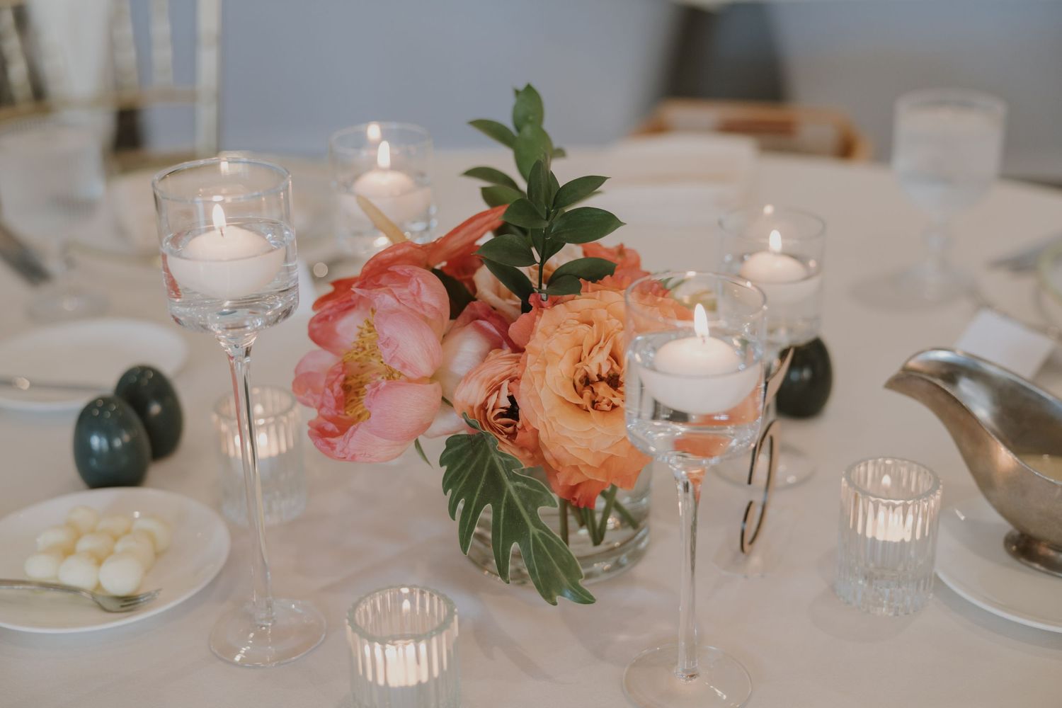 Elegant wedding reception table settings with white linens, candles, and coral floral centerpieces.