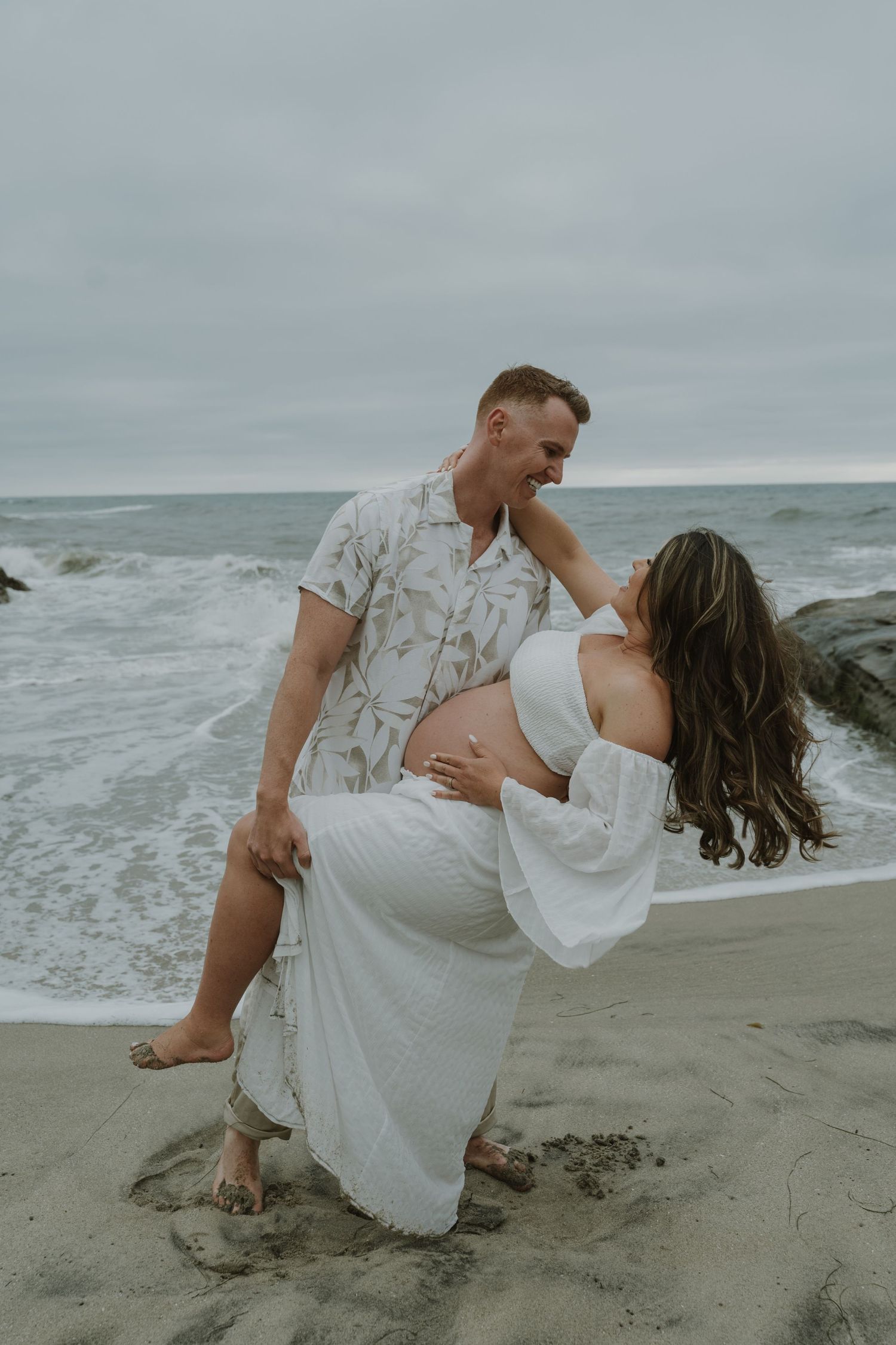 Artistic maternity portraits on a beach with dramatic dips and poses.
