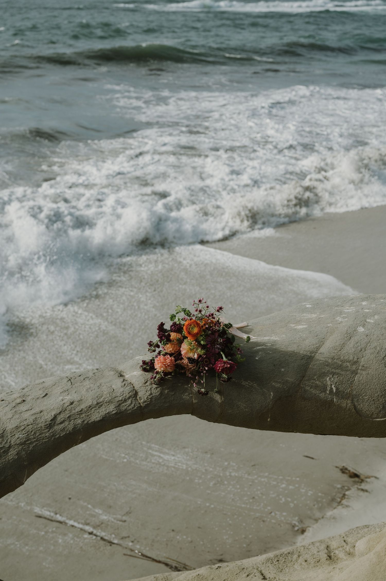A floral bouquet rests on rocky coastal formations with ocean waves in the background.