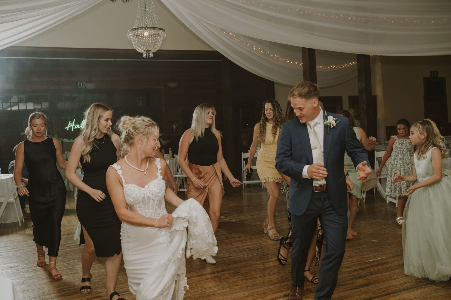Guests dance and celebrate at an indoor wedding reception with white draped ceiling decorations.