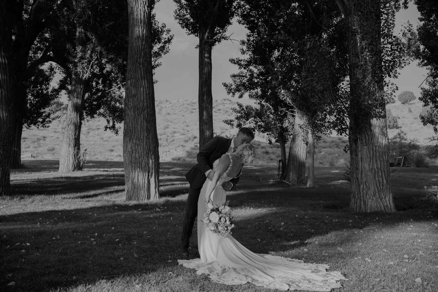 A black and white wedding photo capturing a romantic moment between newlyweds outdoors.