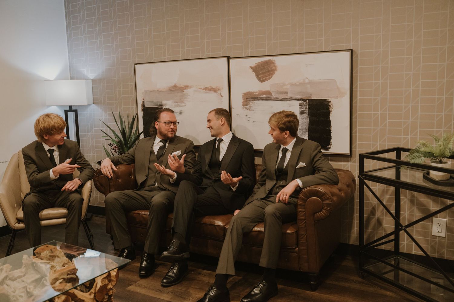 Four men in suits having a conversation while seated on leather furniture in an elegant lounge setting.