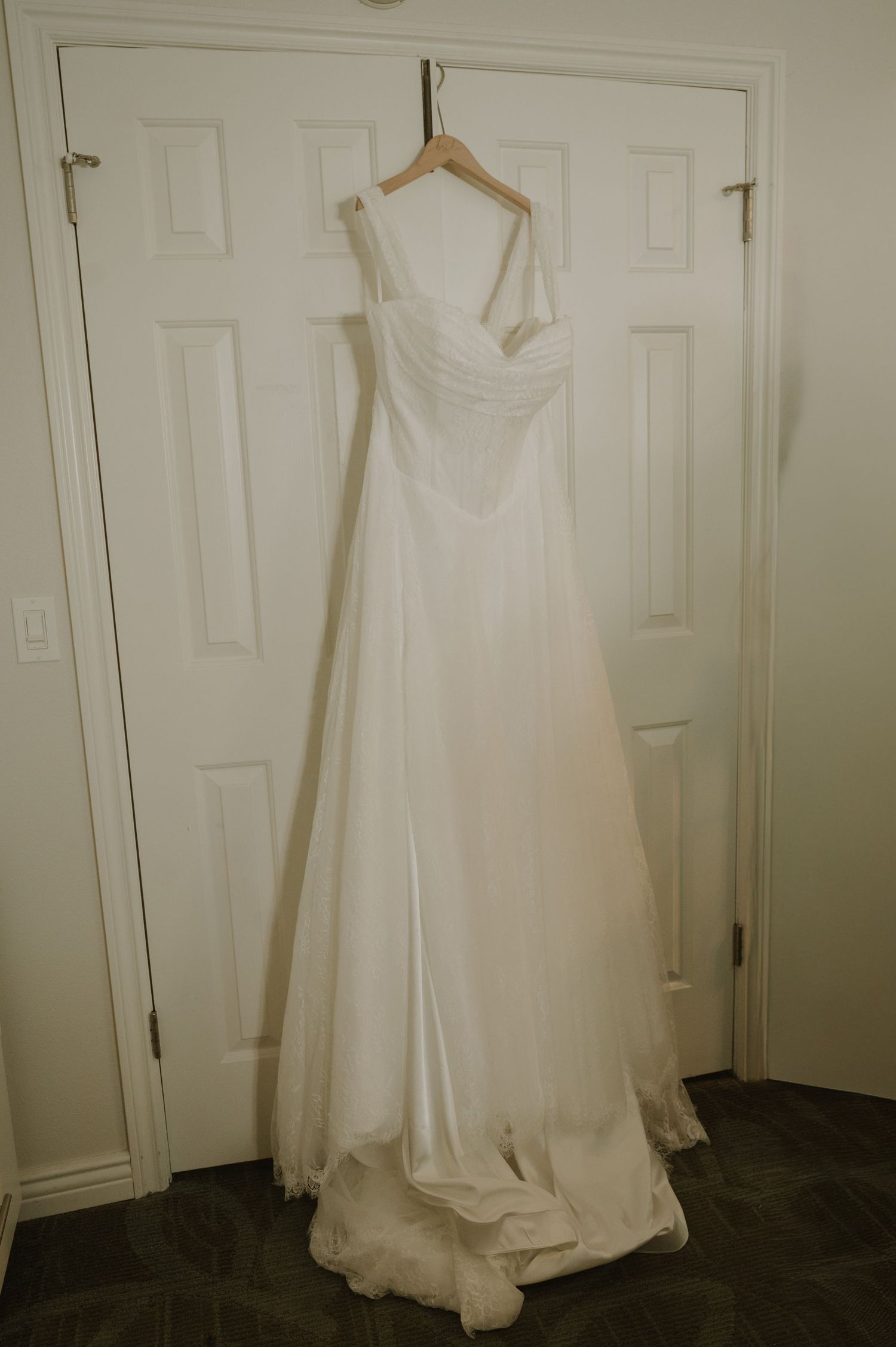 Elegant white A-line wedding gown with sweetheart neckline hanging on a wooden hanger against a white paneled door.