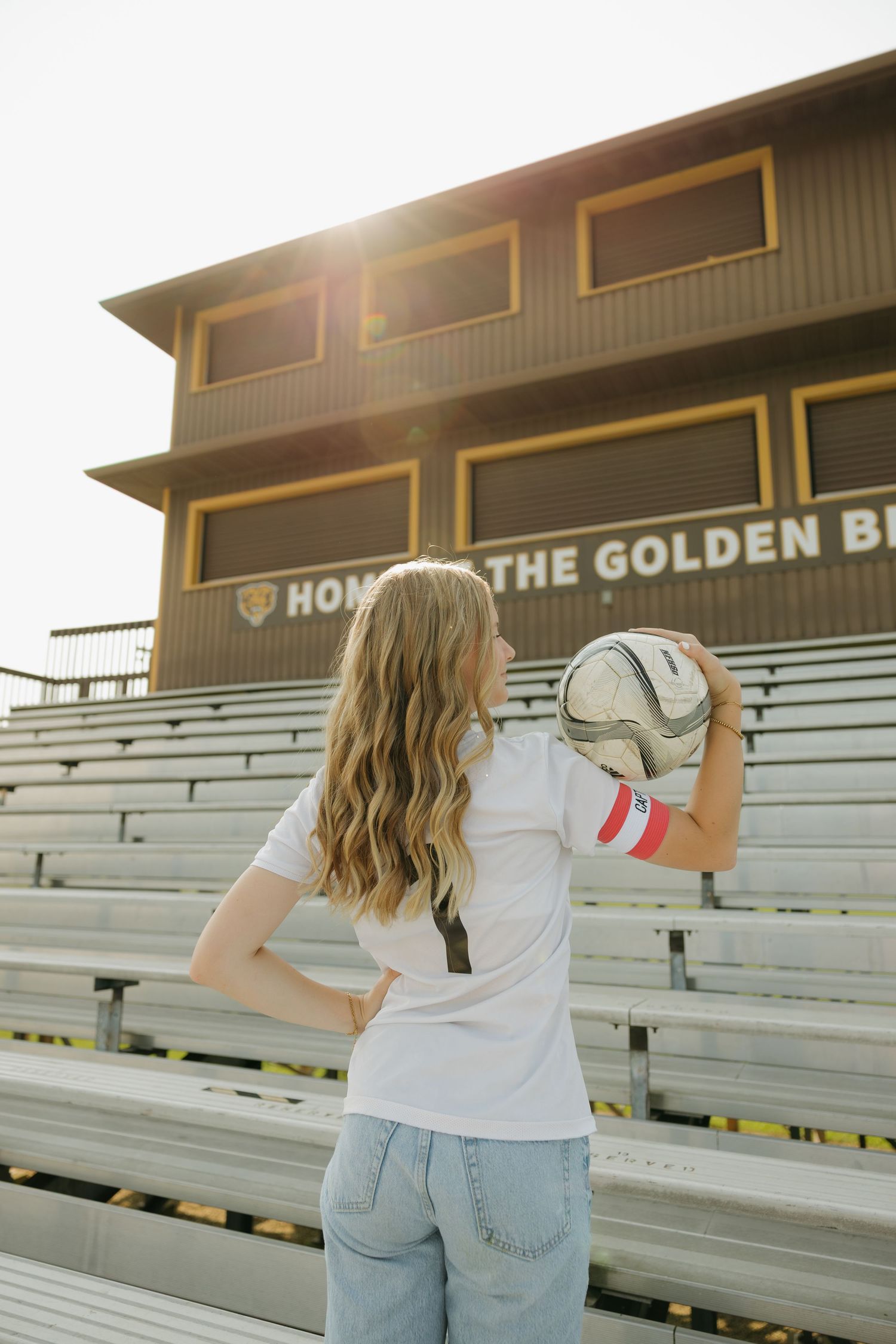 Teenage girl holding a soccer ball on bleachers at Golden Bears stadium in golden hour sunlight.