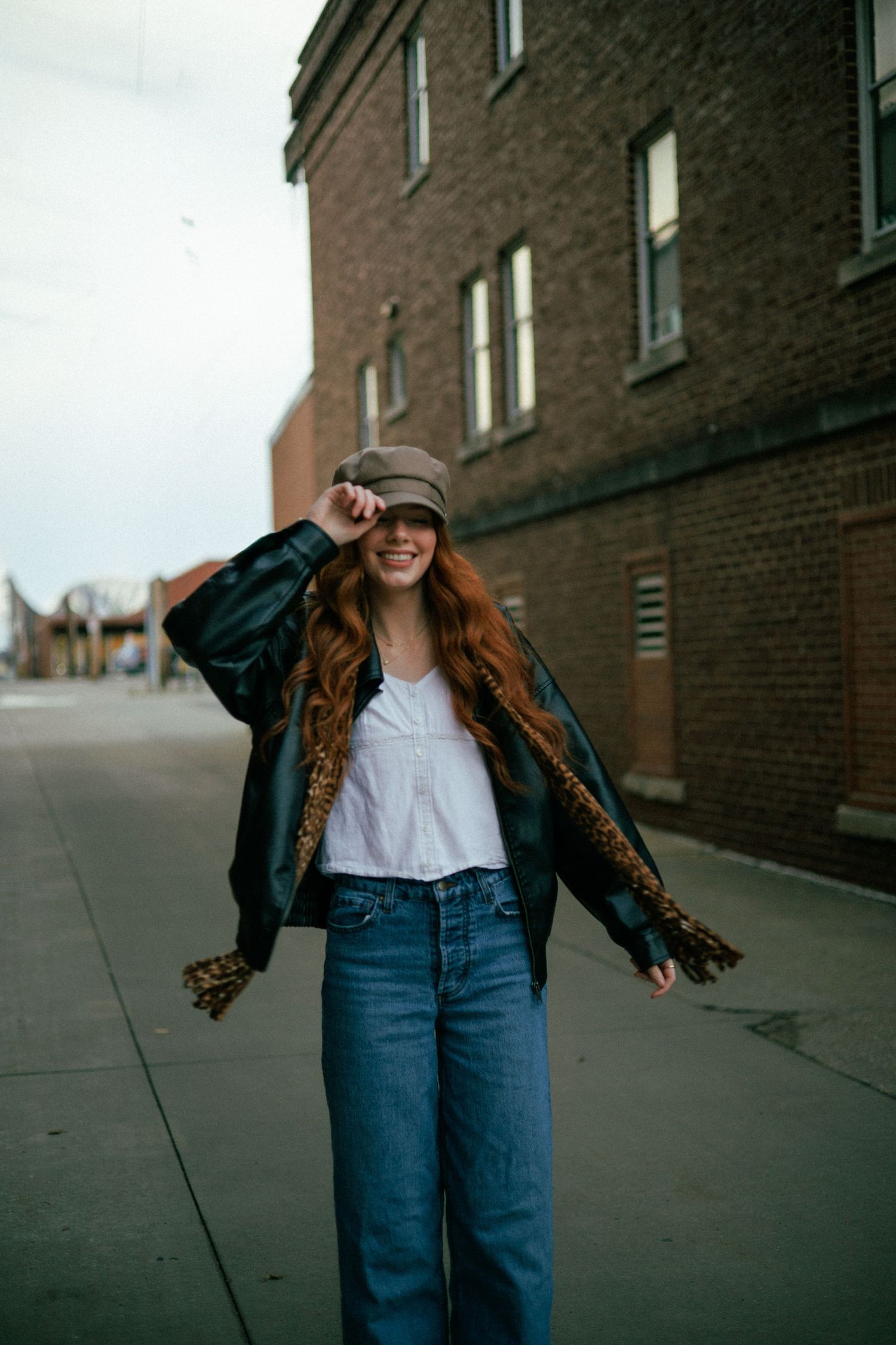 Urban fashion shoot featuring denim, white top and animal print jacket near brick building.