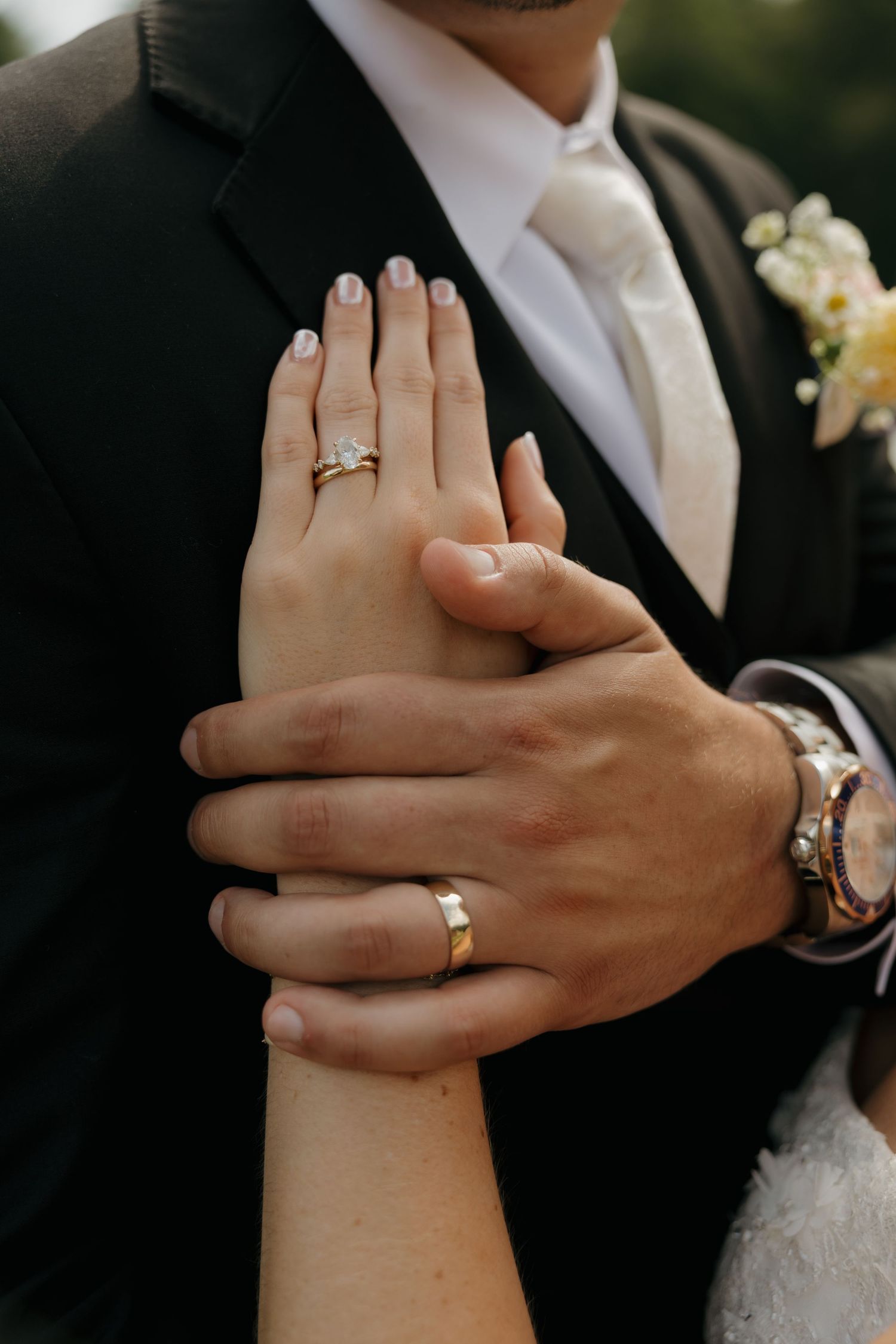 Newlywed couple displaying wedding rings, bride wearing diamond engagement ring, groom with gold band and luxury watch.