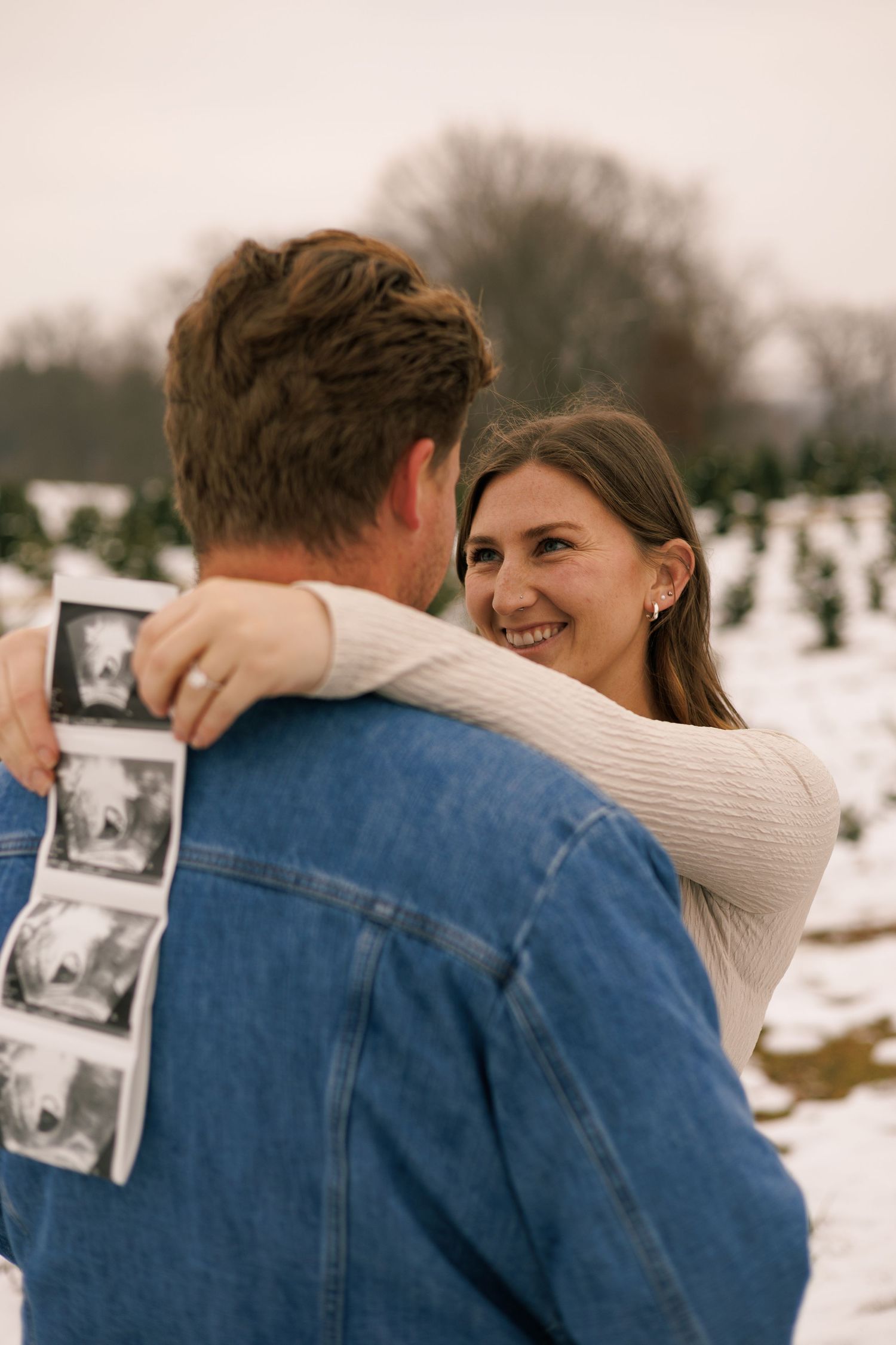 A couple shares an intimate moment while holding a sonogram photo in a snowy setting.