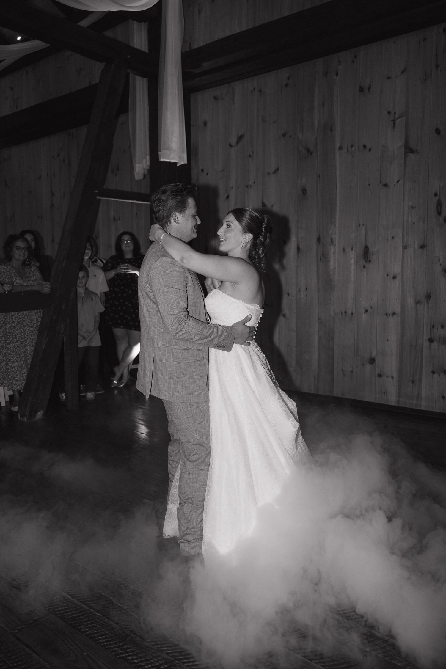 Bride and groom share a first dance surrounded by low-lying fog on a rustic barn wedding dance floor in black and white.