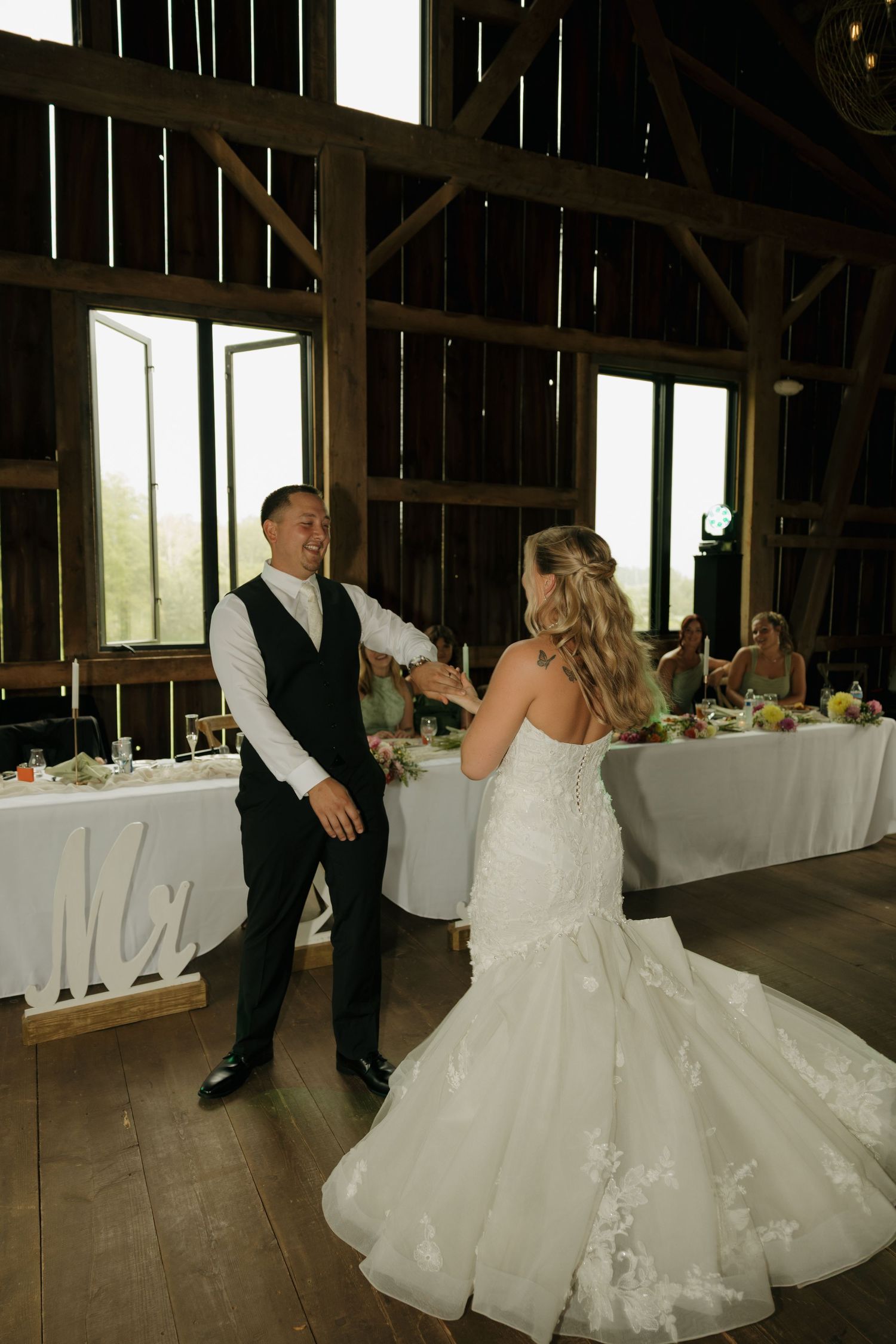 Bride and groom share their first dance in a rustic barn venue with wooden beams and warm lighting.