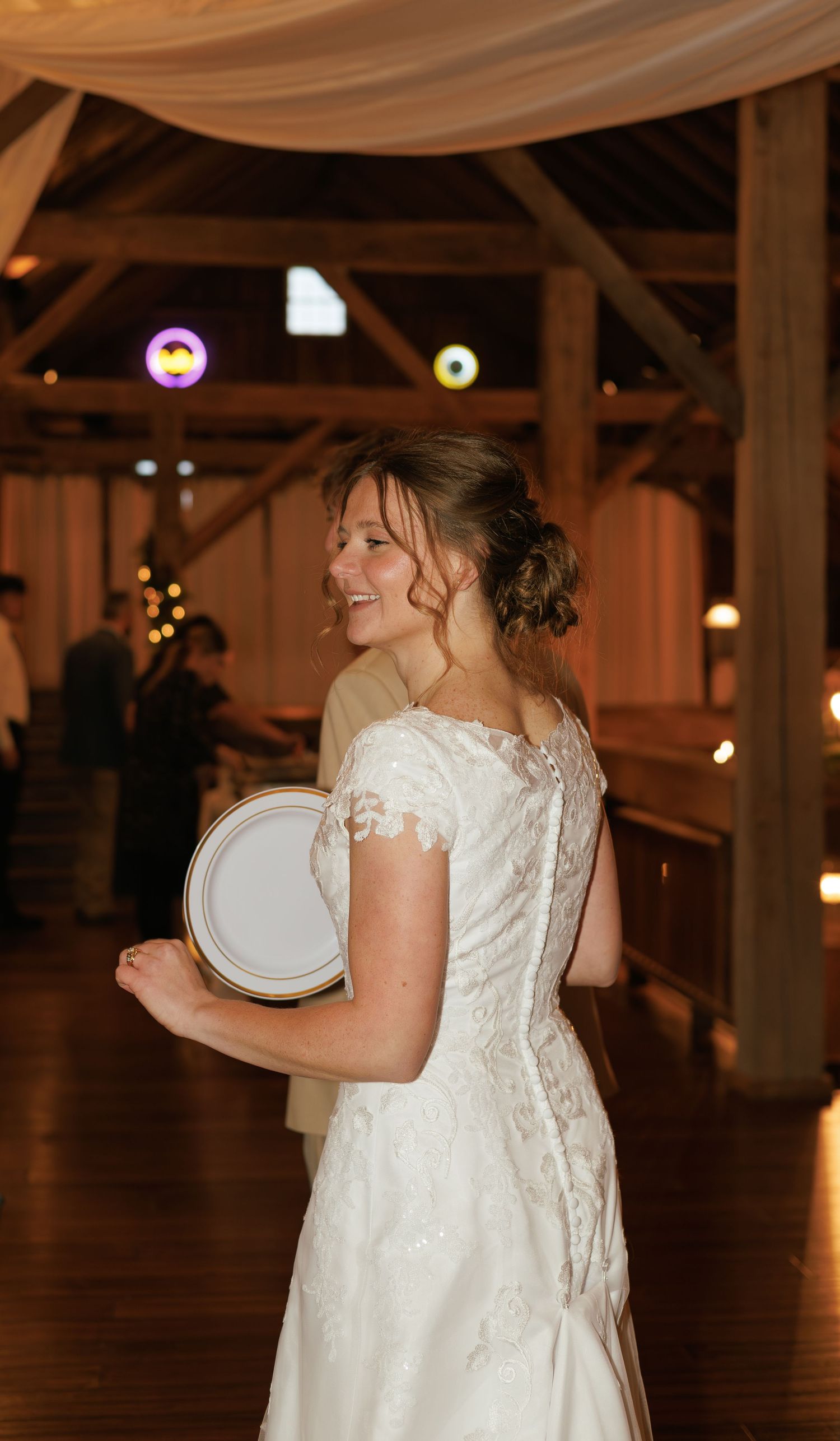 Wedding reception in a barn venue with white fabric draping and warm lighting.