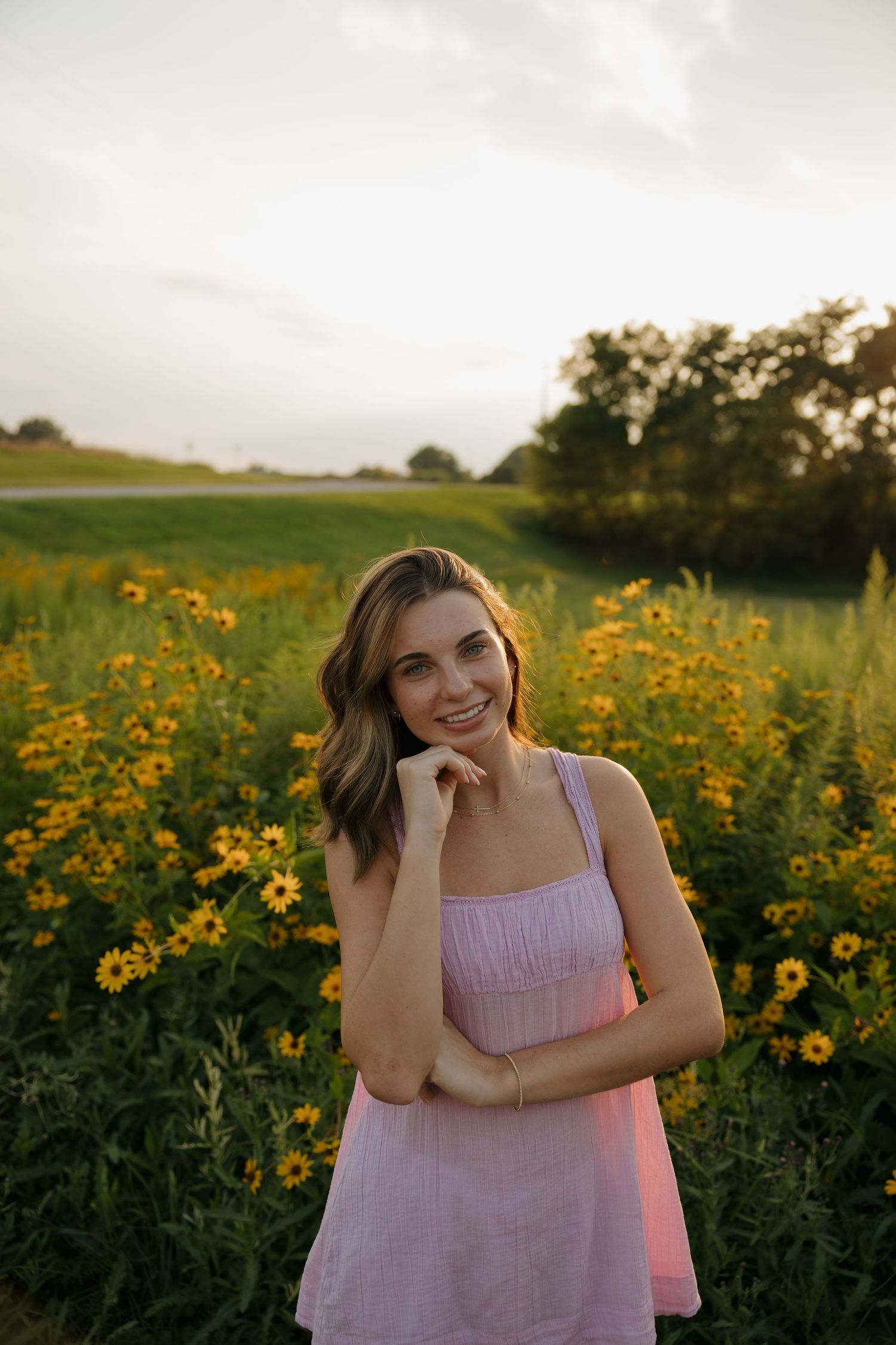 Young woman in pink dress smiling in a vibrant field of yellow wildflowers at golden hour.