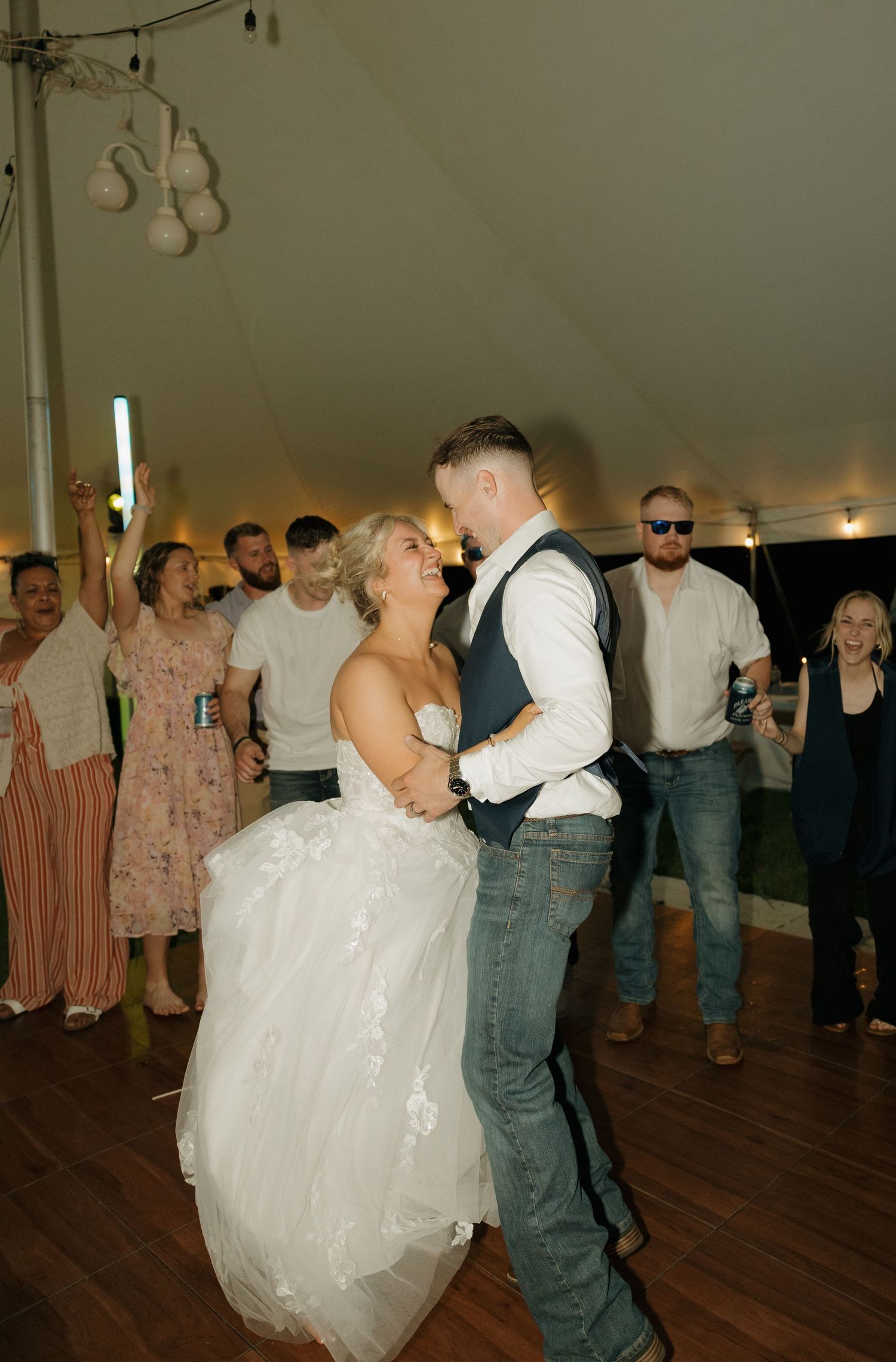 Bride and groom sharing romantic dance moment with cheering guests surrounding them at wedding reception.