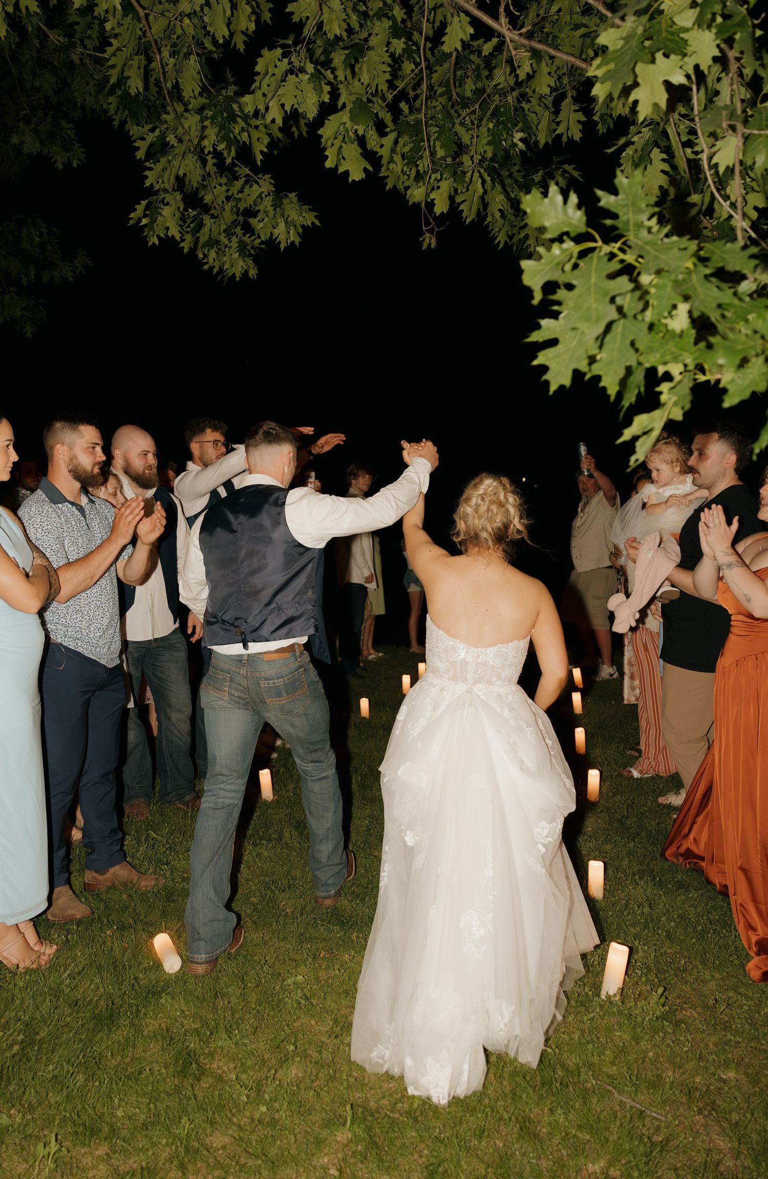 Bride and groom dancing through a candlelit guest sendoff line at night outdoors.