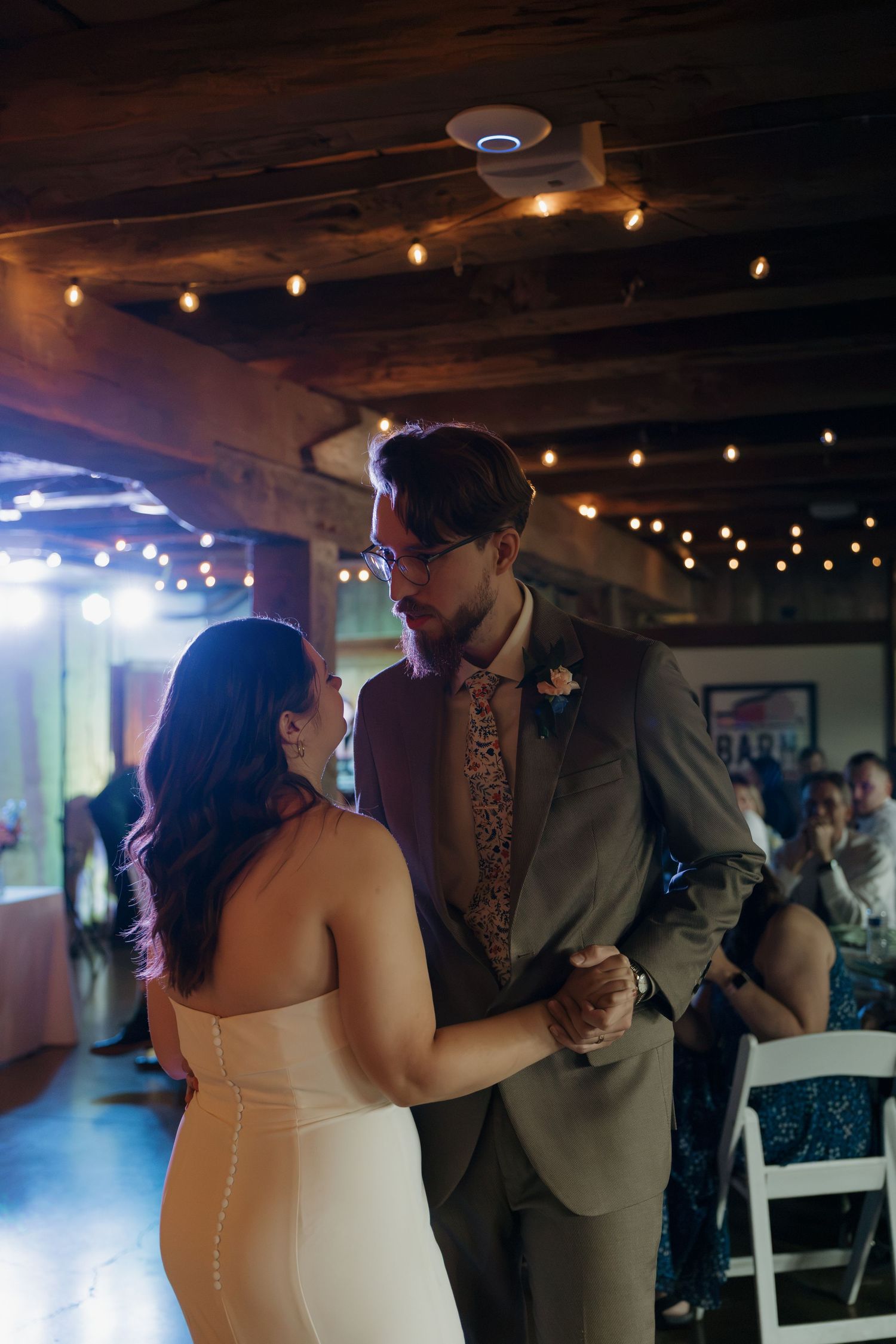 Bride and groom share their first dance in a rustic barn venue adorned with string lights during their wedding reception.