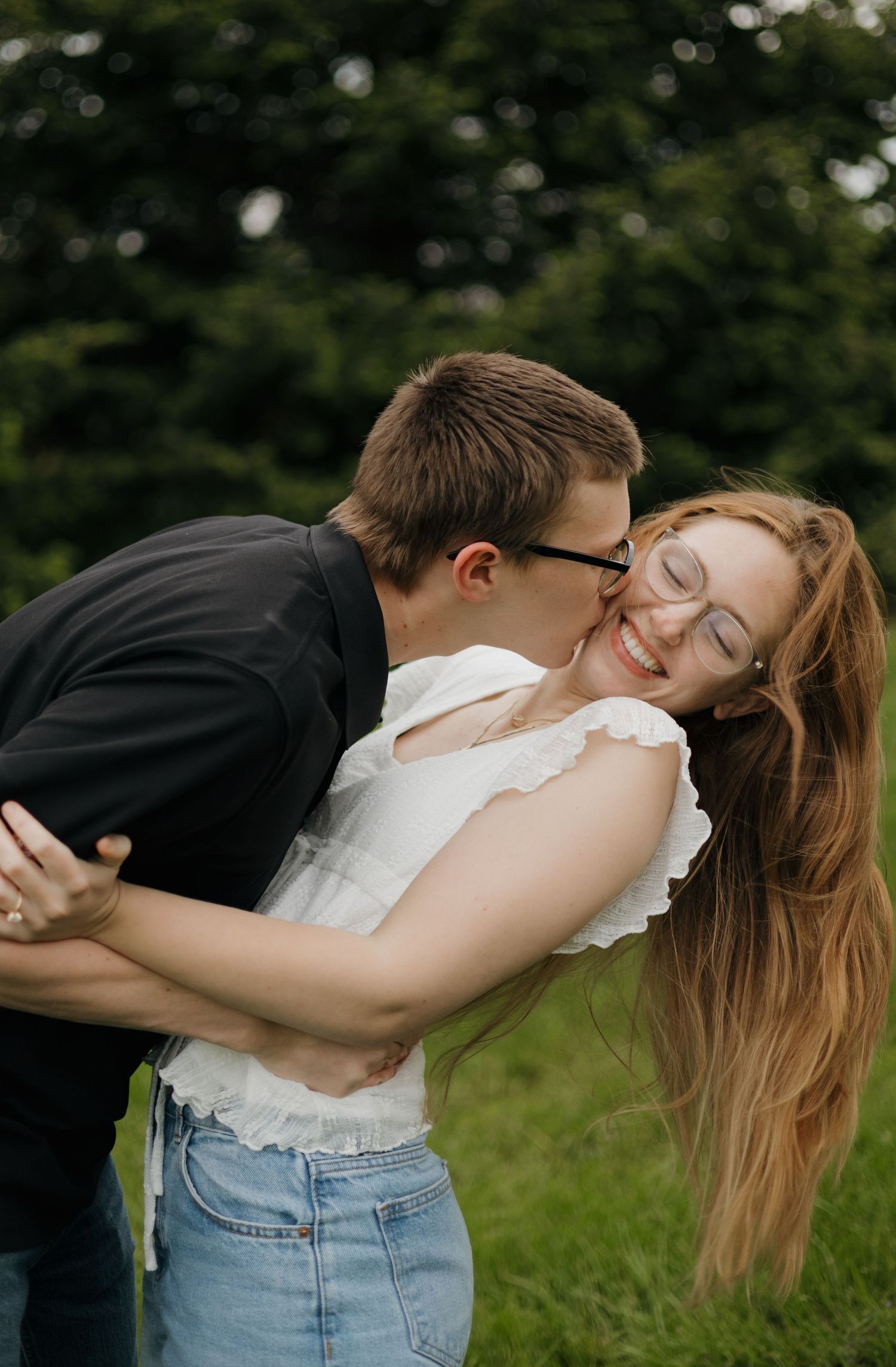 A young couple shares a romantic moment outdoors, as a man kisses a smiling redhead woman in a white top.