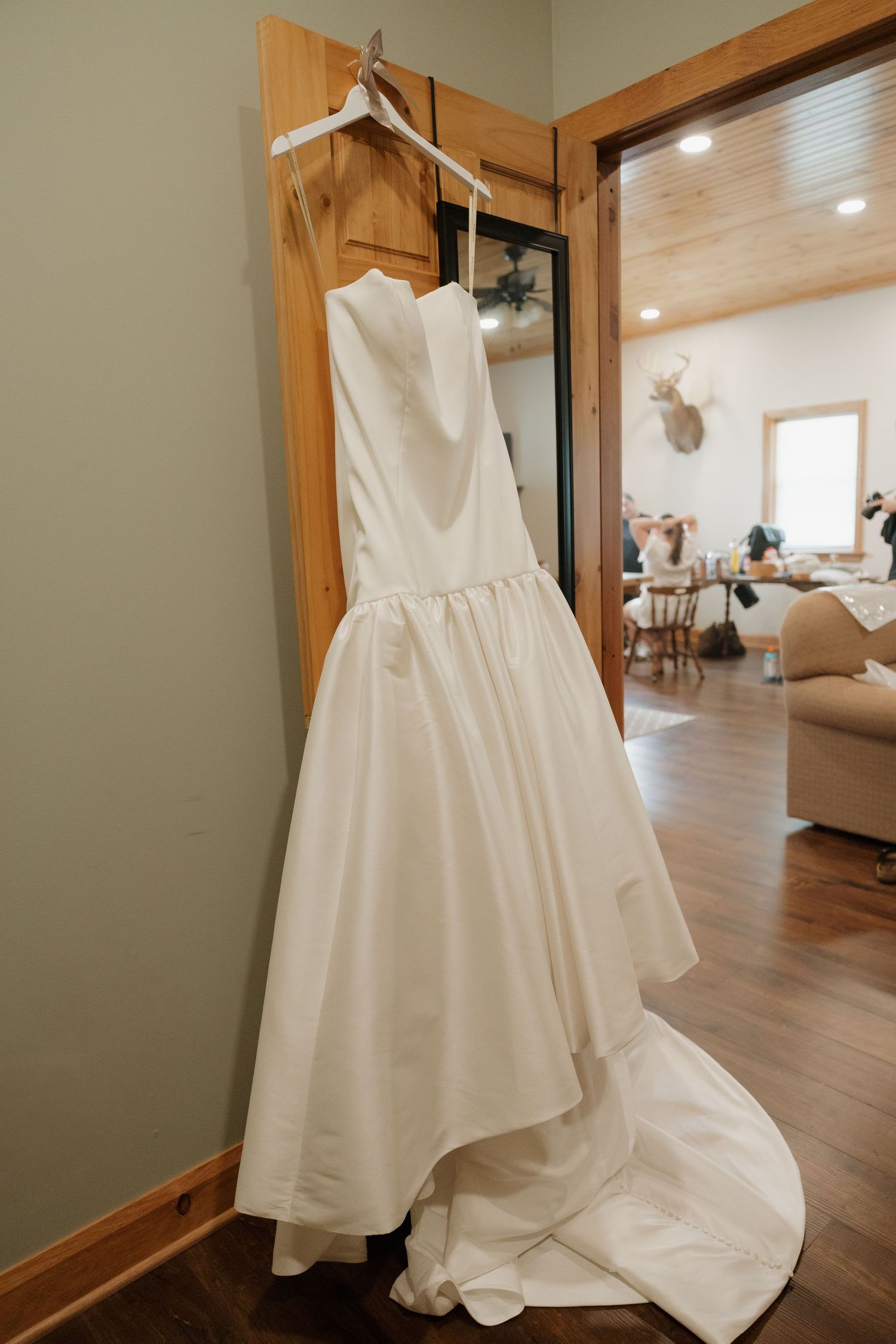 Elegant white strapless wedding dress with a long train hanging on a wooden door in a rustic venue.