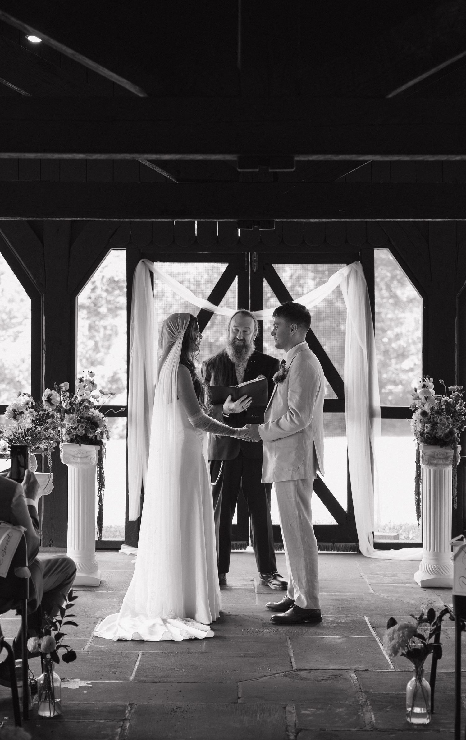 Black and white photo of a bride and groom exchanging vows at an elegant outdoor pavilion wedding ceremony.