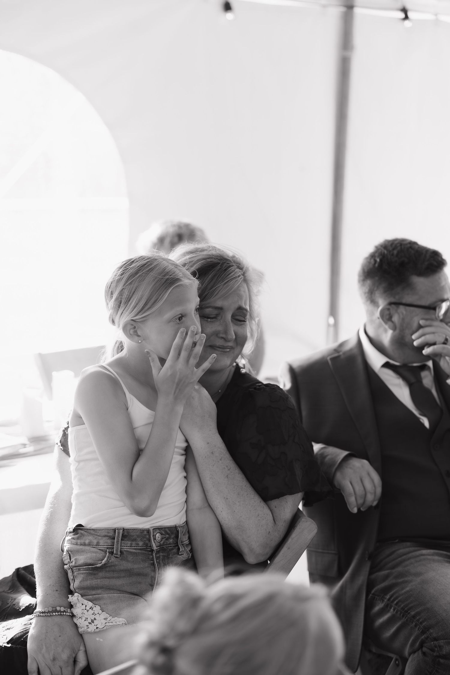 Black and white photo of emotional woman and girl embracing, wiping tears at a wedding ceremony.
