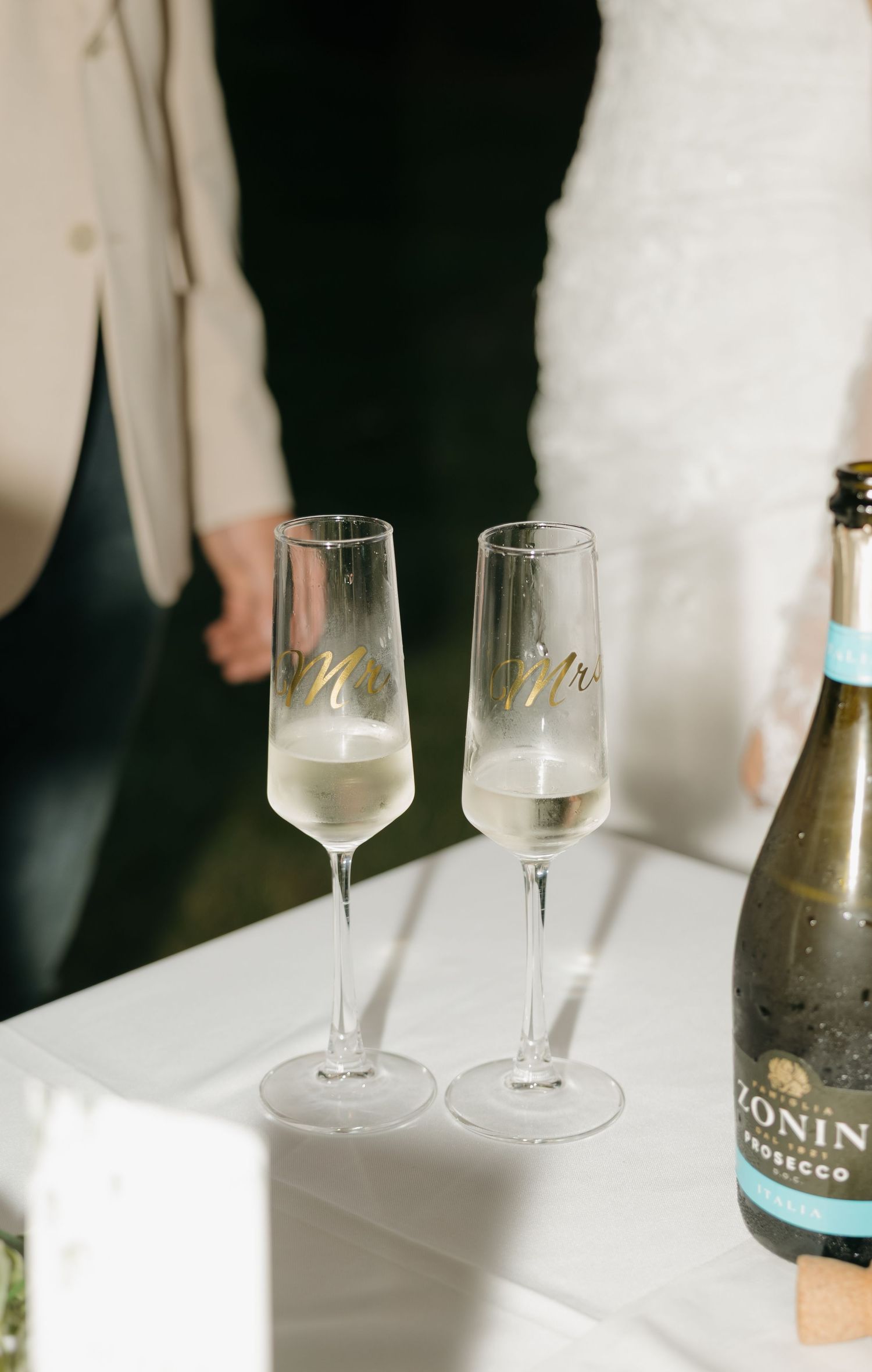 Mr. and Mrs. champagne flutes filled with prosecco beside a Zonin bottle at a wedding reception.