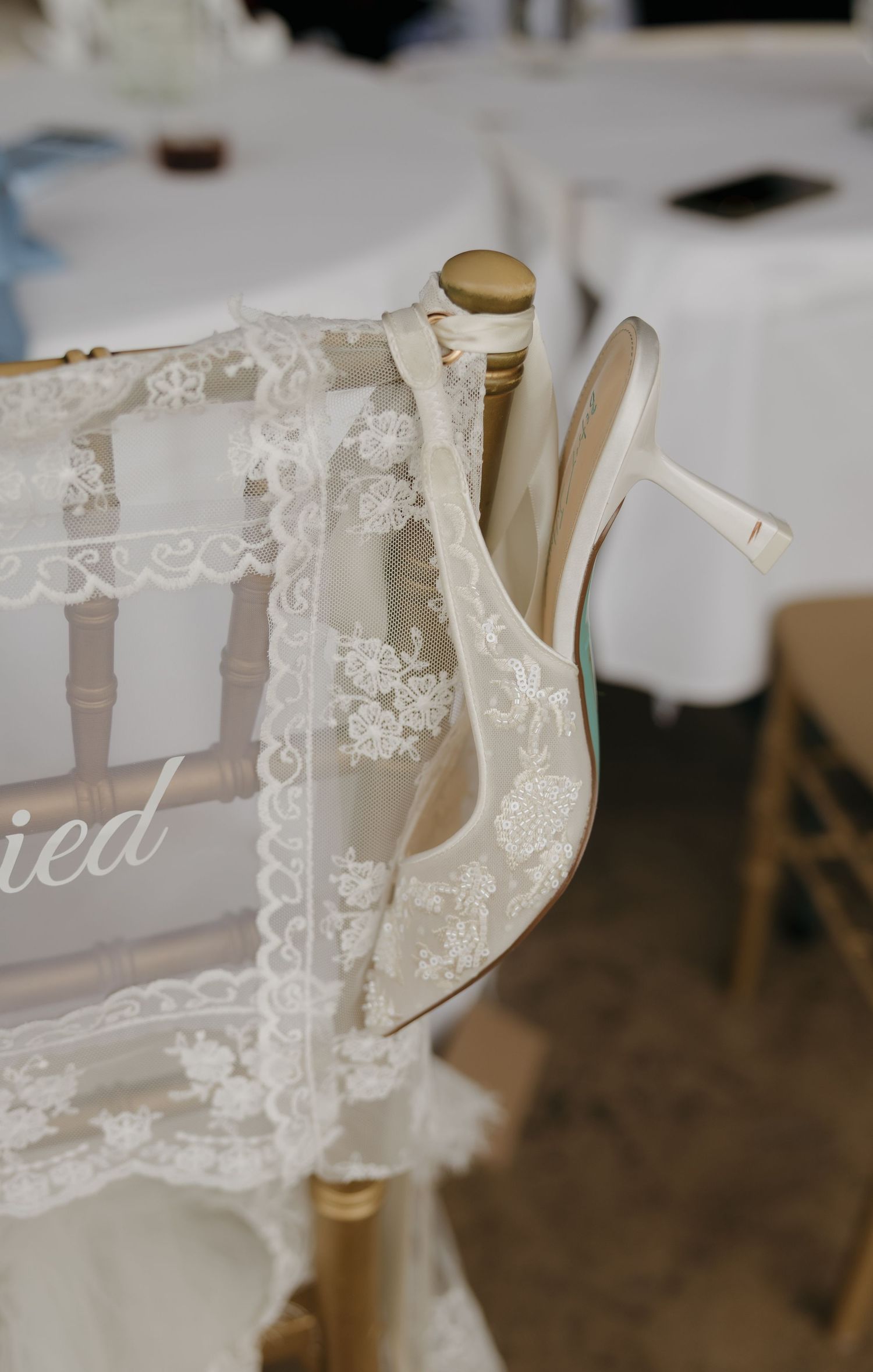 White lace wedding veil and bridal heels draped over a gold chiavari chair at an elegant wedding reception.