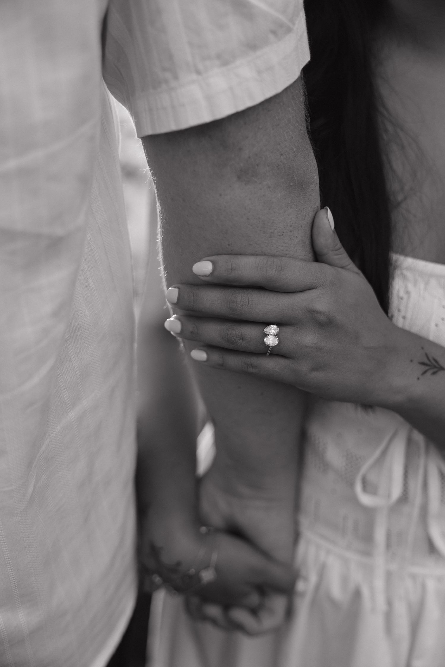 Black and white photo of a couple holding hands, woman wearing an elegant engagement ring with manicured nails.
