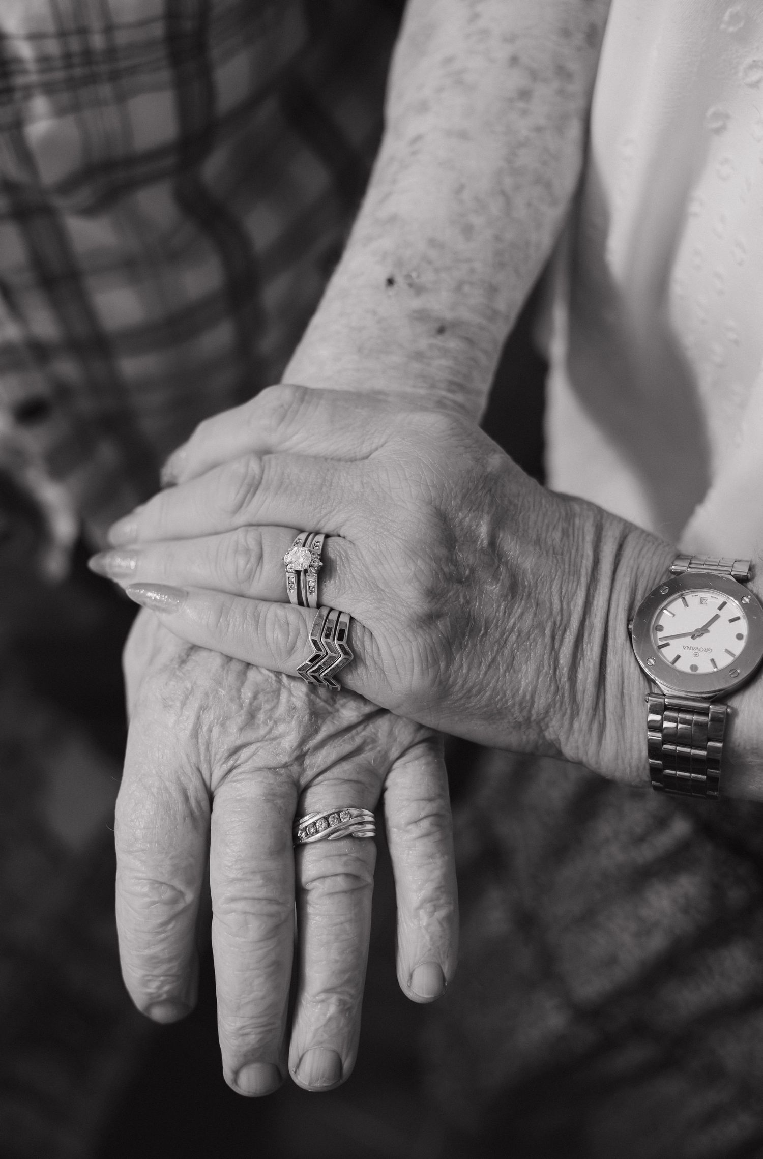Black and white photo of elderly couple holding hands, wearing rings and a watch, symbolizing enduring love.