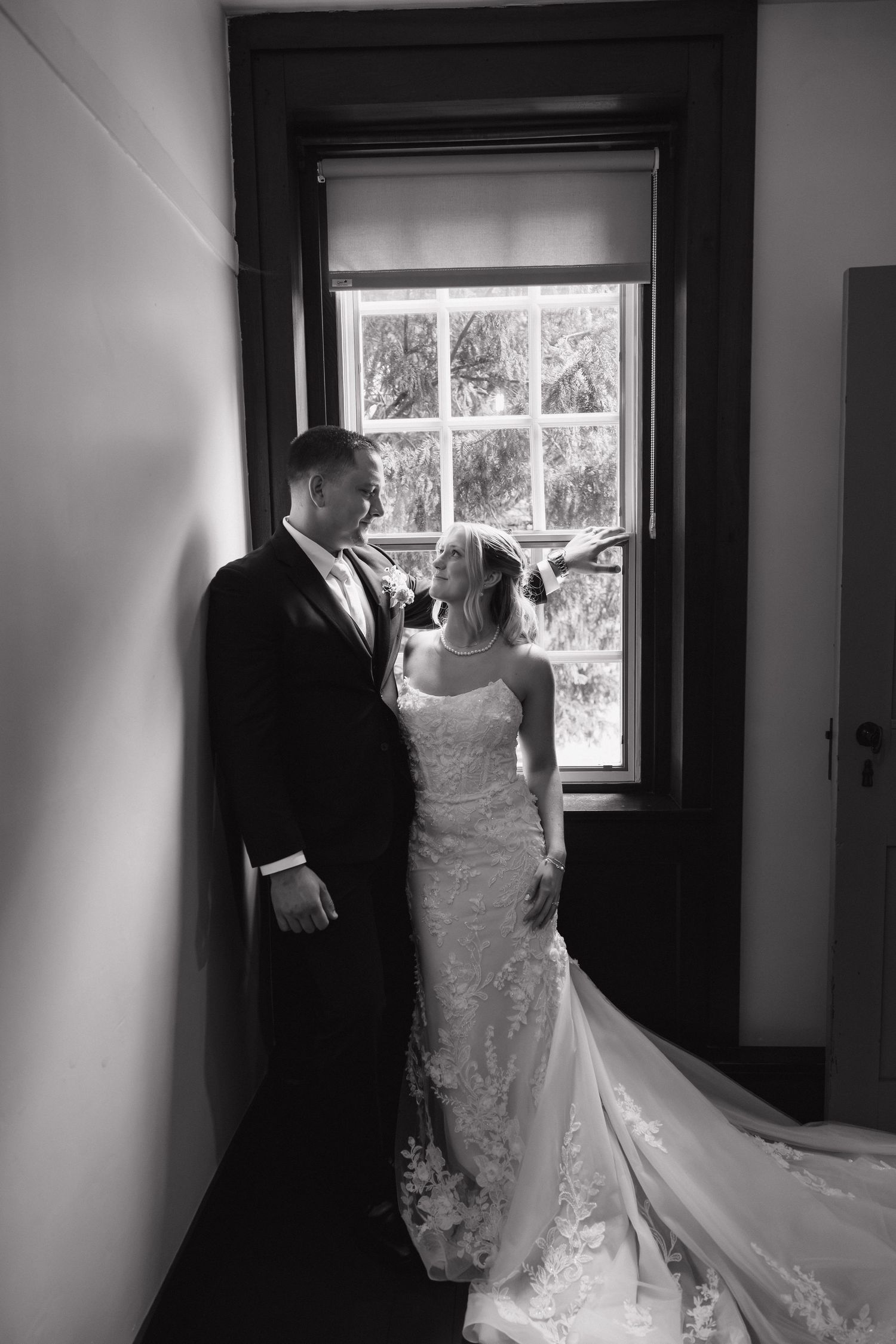 Bride and groom share an intimate moment by a window in a black and white wedding portrait indoors.