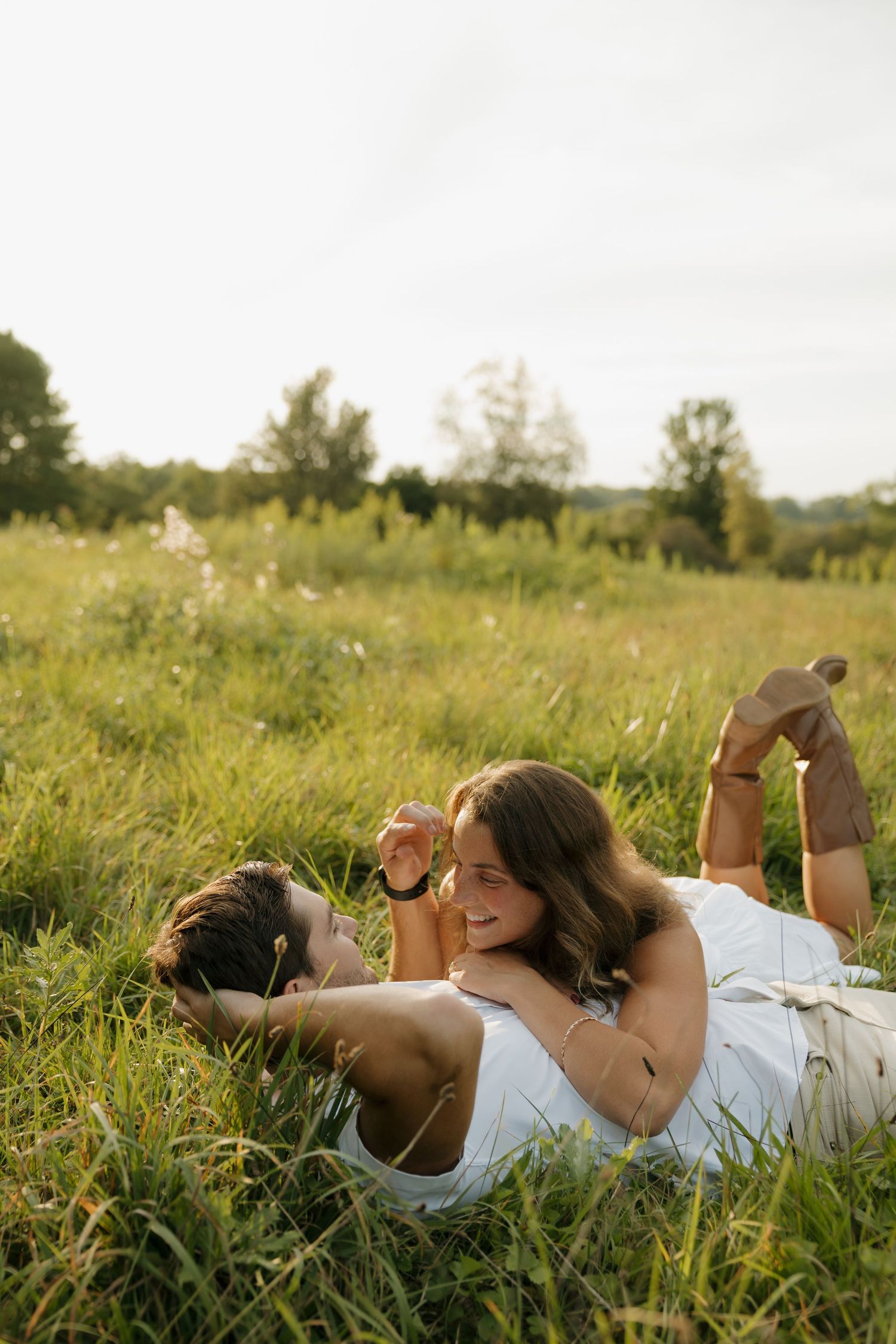 Couple lying in a sunny green meadow, smiling and relaxing together on a warm summer day.