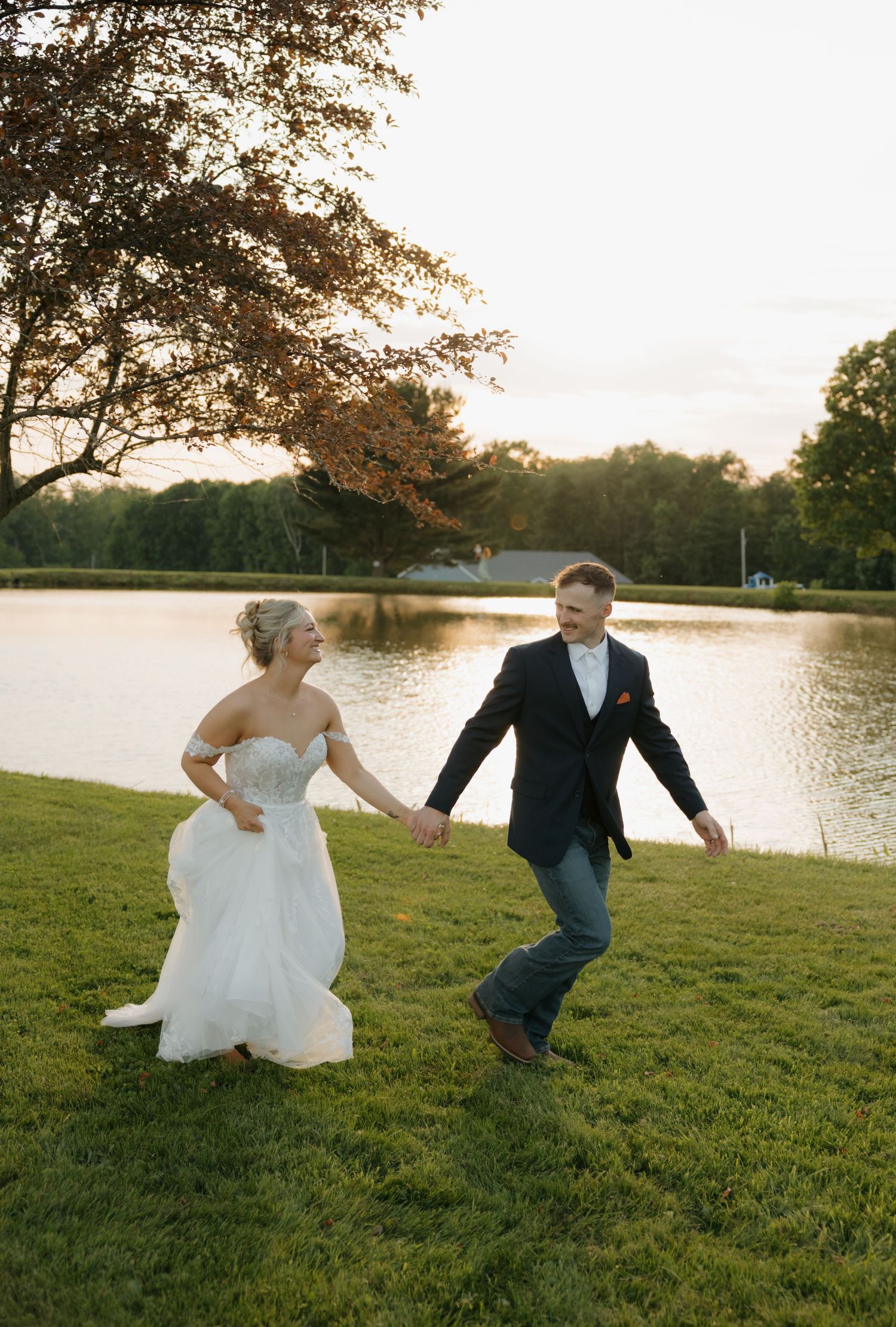 Bride and groom holding hands walking by a lake at sunset during golden hour.
