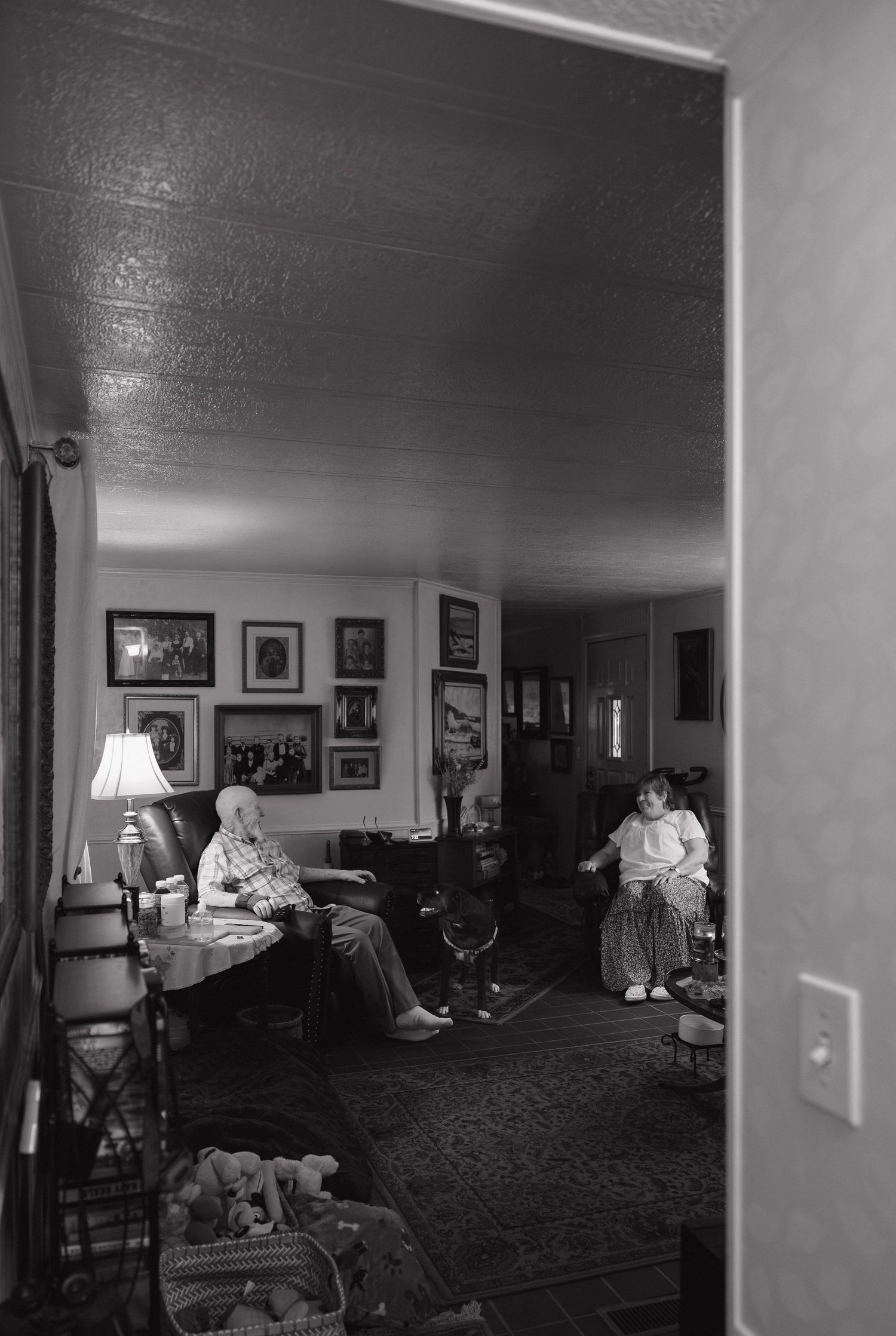Black and white photo of elderly person and child relaxing in a cozy living room with framed photos on walls.