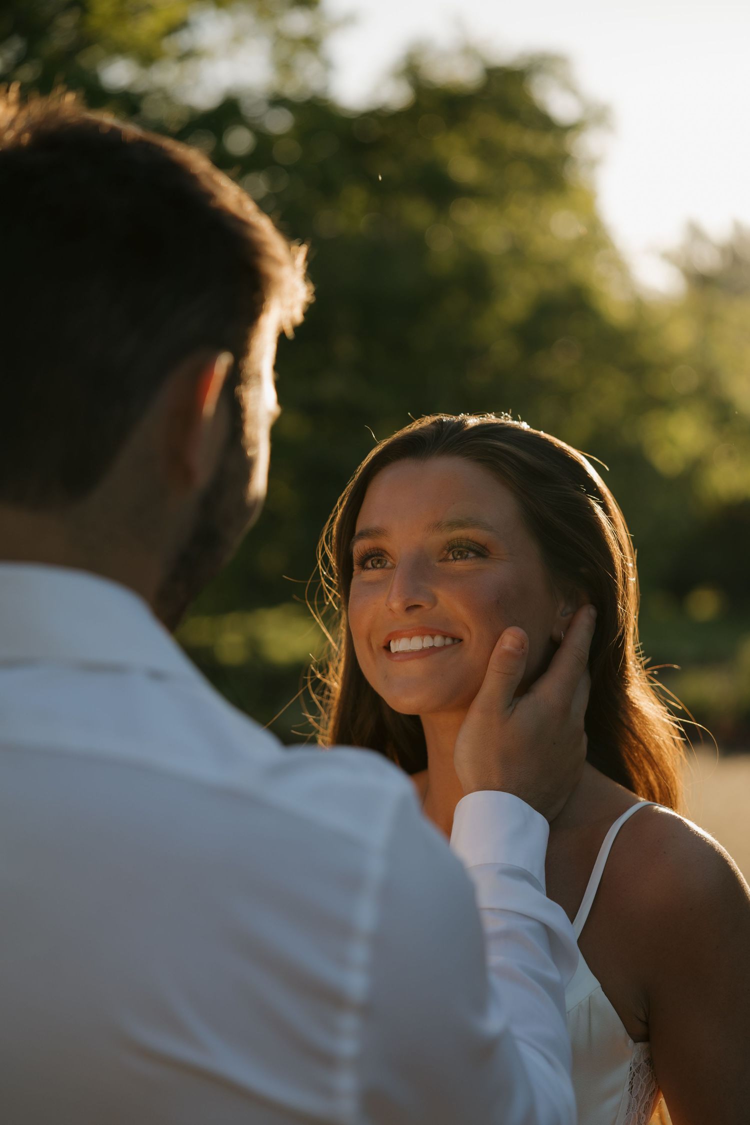 A groom tenderly touches his bride's face during a golden hour outdoor wedding portrait.