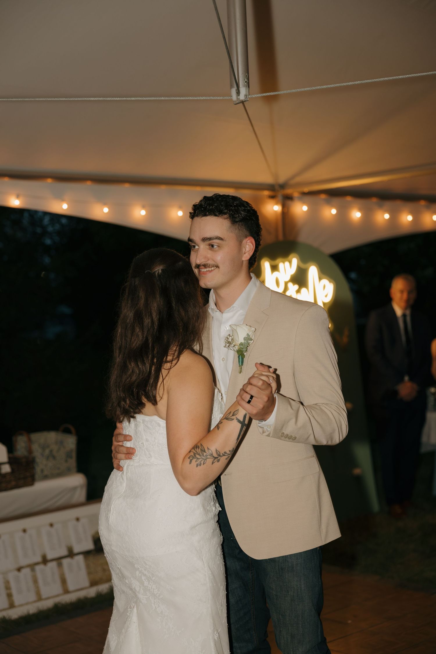 Bride and groom share their first dance under string lights at an outdoor wedding reception tent.
