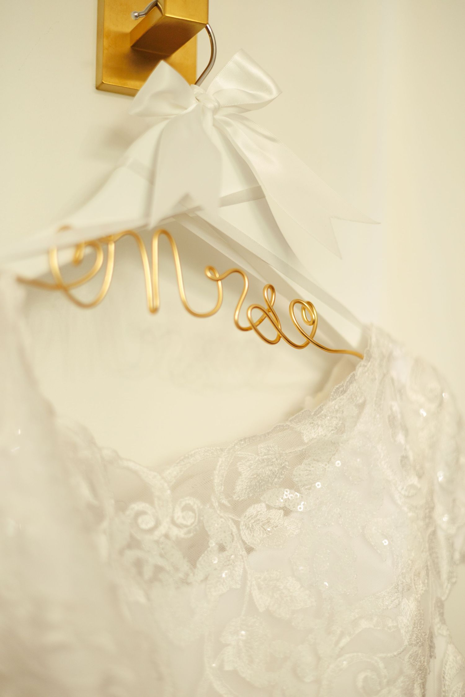 Close-up of a delicate white wedding dress with lace details hanging on a gold hanger.