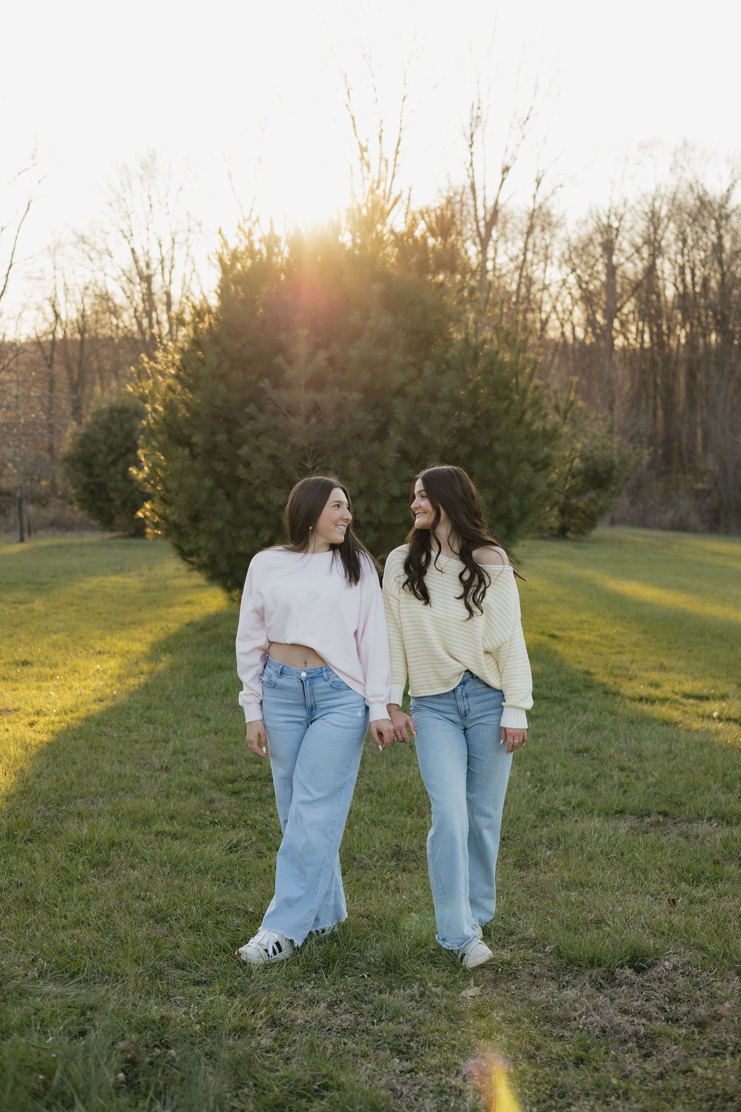 Two people in matching outfits walking together in a sunlit field during golden hour.