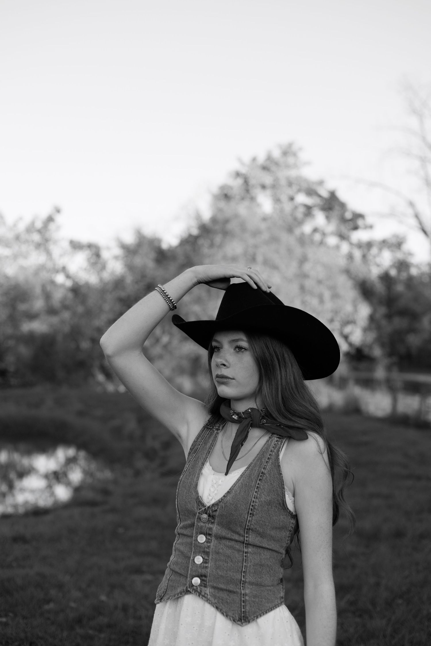 A series of black and white portraits showing someone in a denim vest and wide-brimmed hat in a pastoral setting.